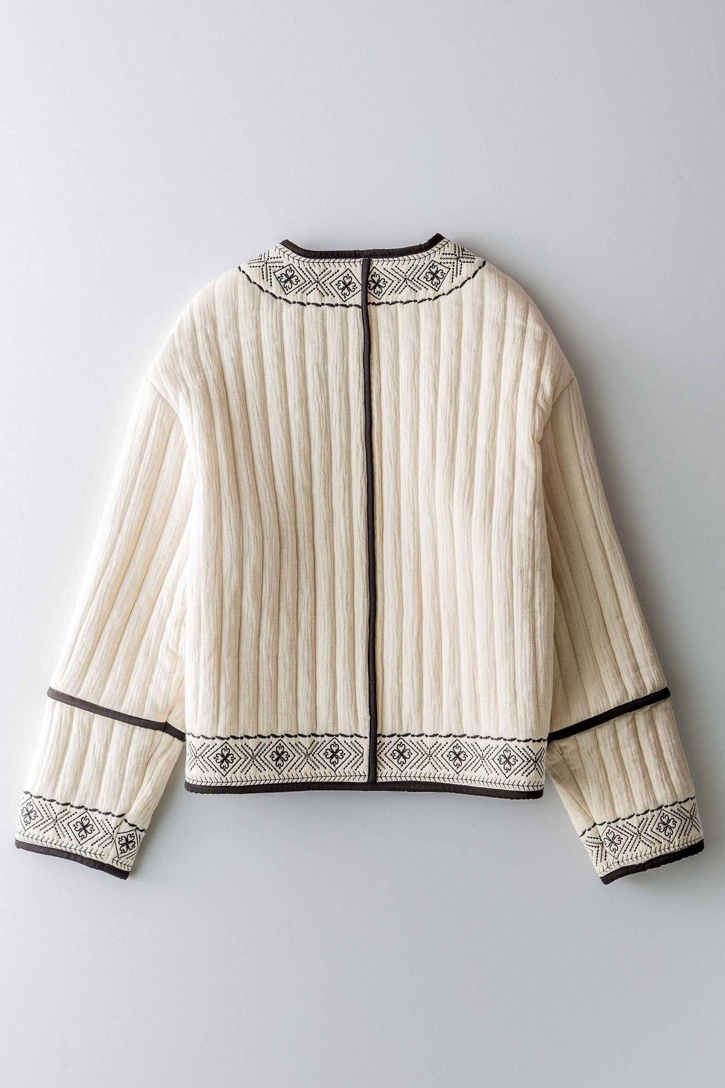 boho quilted ivory jacket with black exposed seam detailing and design along hem, has pockets, 2 clasp enclosure