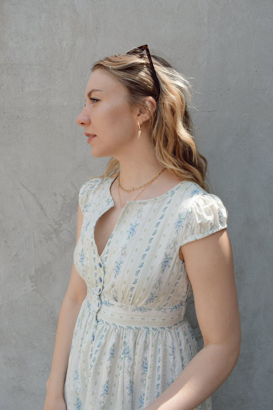 cap sleeve midi dress with ditsy floral pattern and blue buttons down the front until hitting a slit in front hem, fitted waist with smocked band in back, v neck, twirly