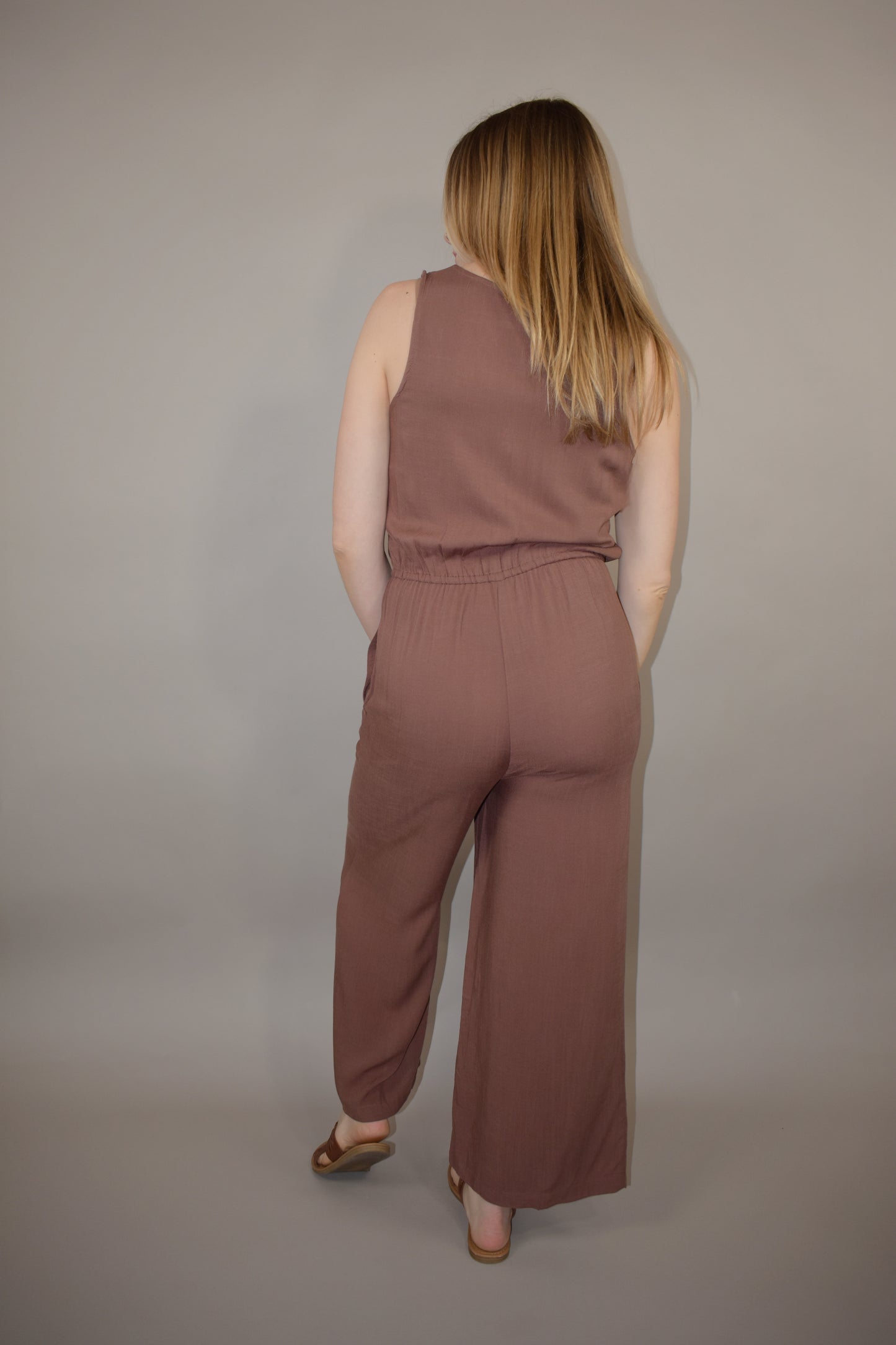 v neck jumpsuit with thin elastic waistband and drawstring with wooden bead at the end has pockets wide leg and buttons down the front of bodice