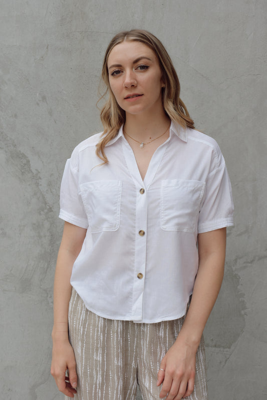 white linen button down, short sleeve, v neck with collar, 3 brown buttons, patch breast pockets, scoop hemline, button detail on back of sleeve cuff