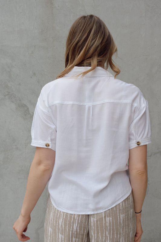 white linen button down, short sleeve, v neck with collar, 3 brown buttons, patch breast pockets, scoop hemline, button detail on back of sleeve cuff
