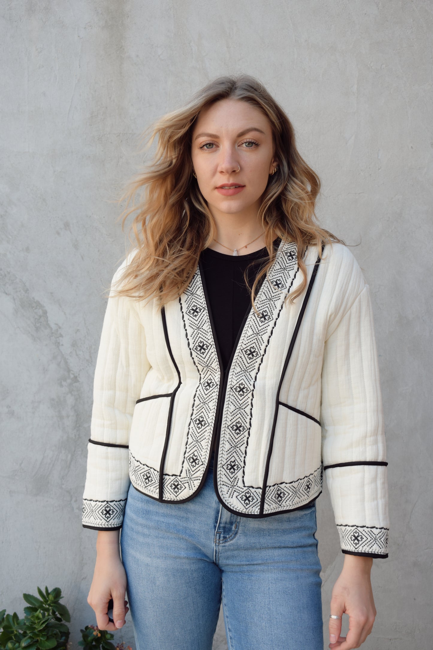 boho quilted ivory jacket with black exposed seam detailing and design along hem, has pockets, 2 clasp enclosure