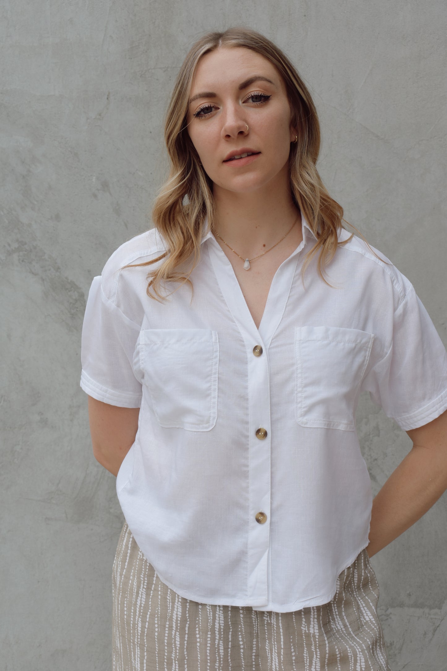 white linen button down, short sleeve, v neck with collar, 3 brown buttons, patch breast pockets, scoop hemline, button detail on back of sleeve cuff