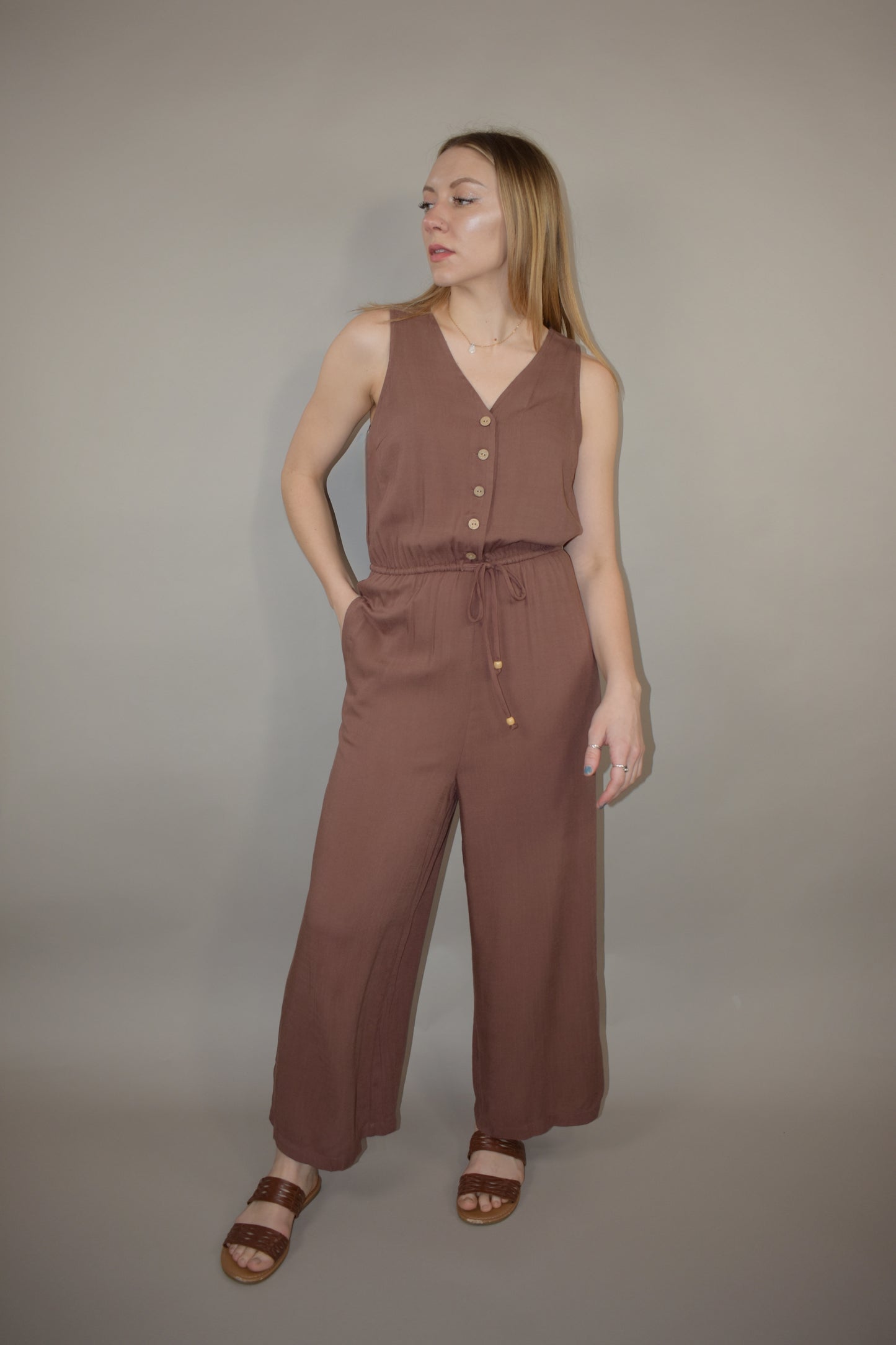 v neck jumpsuit with thin elastic waistband and drawstring with wooden bead at the end has pockets wide leg and buttons down the front of bodice