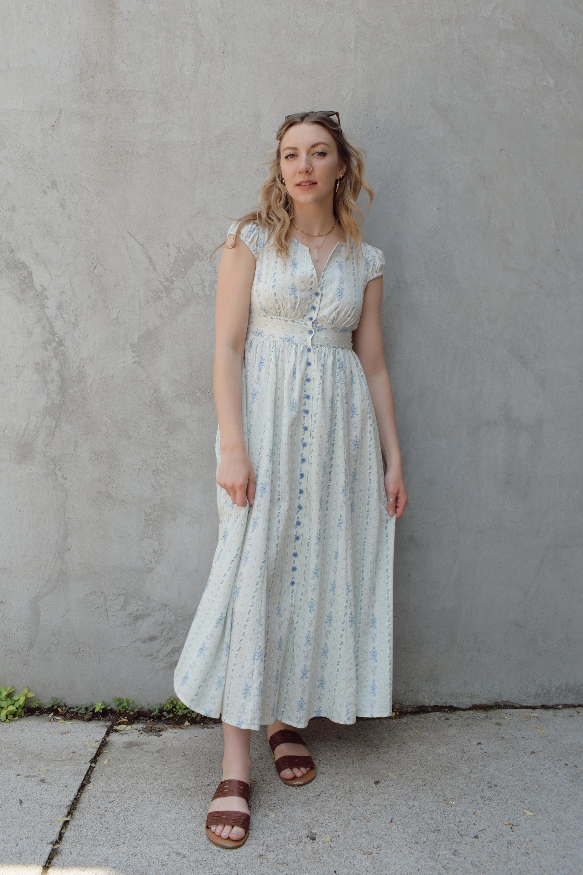 cap sleeve midi dress with ditsy floral pattern and blue buttons down the front until hitting a slit in front hem, fitted waist with smocked band in back, v neck, twirly
