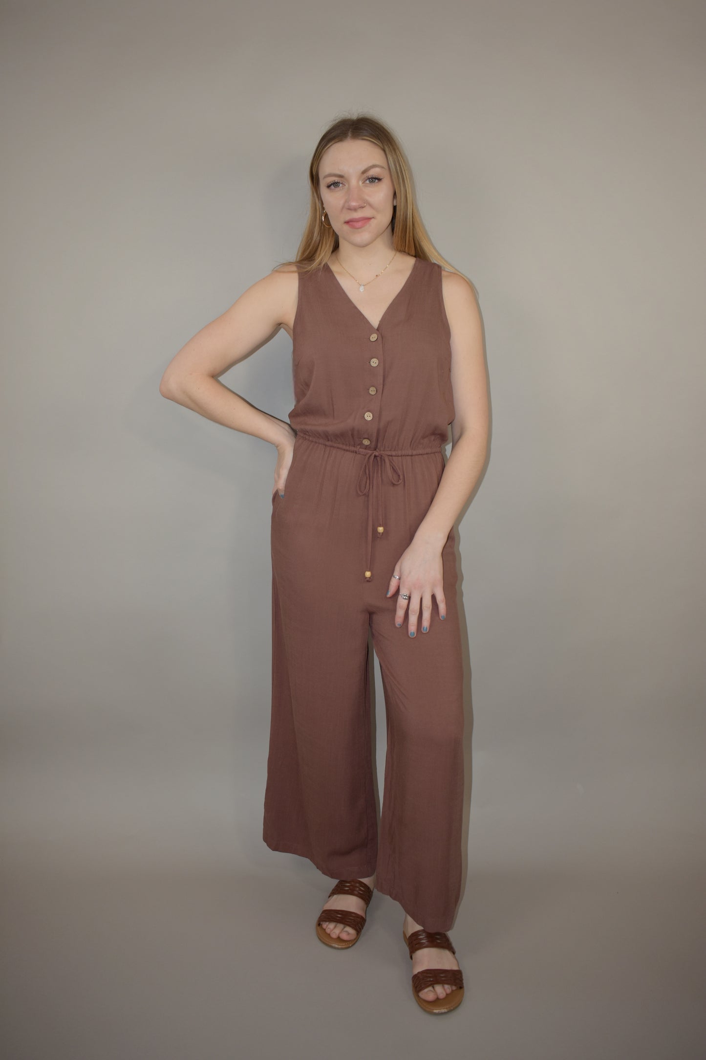 v neck jumpsuit with thin elastic waistband and drawstring with wooden bead at the end has pockets wide leg and buttons down the front of bodice