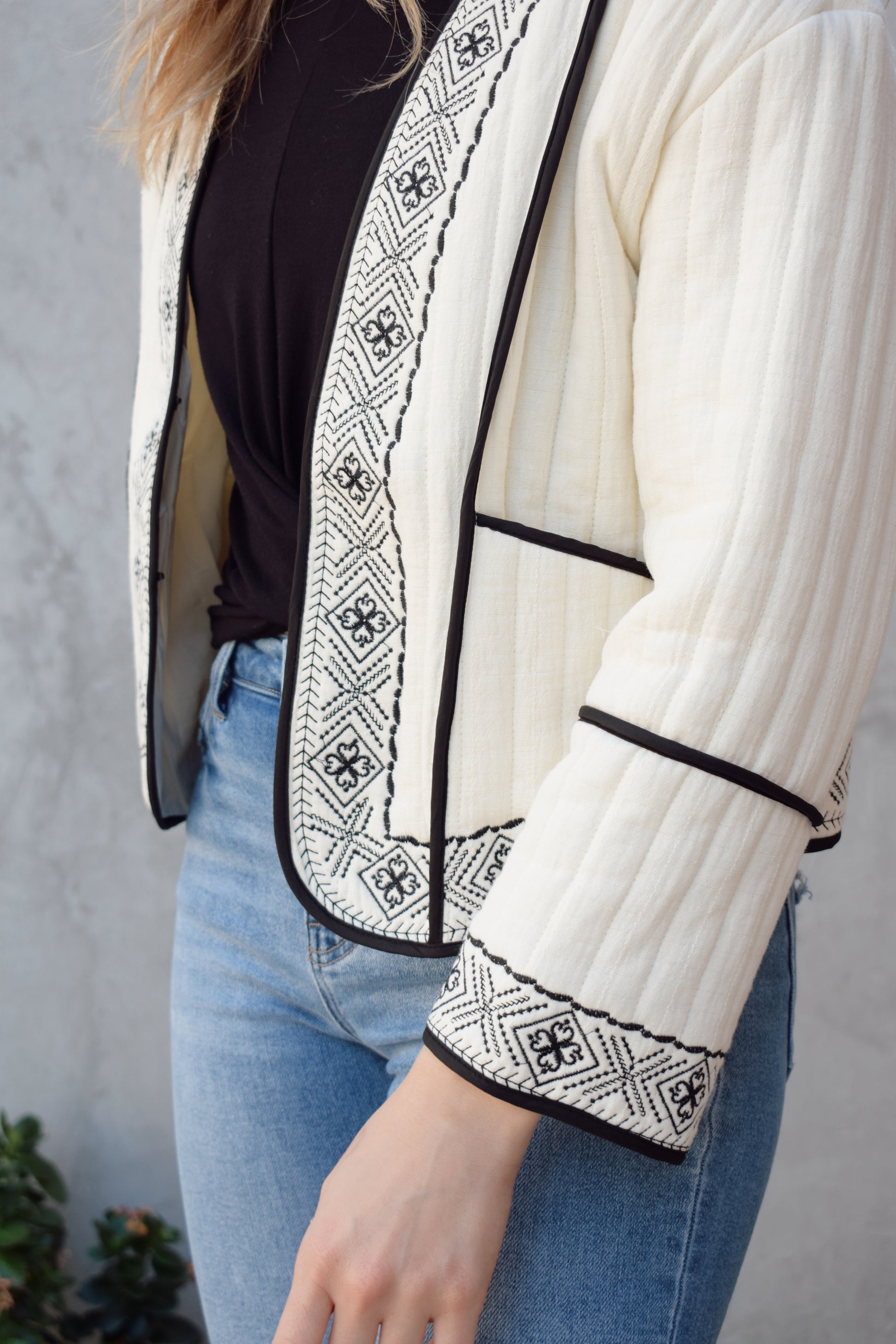 boho quilted ivory jacket with black exposed seam detailing and design along hem, has pockets, 2 clasp enclosure