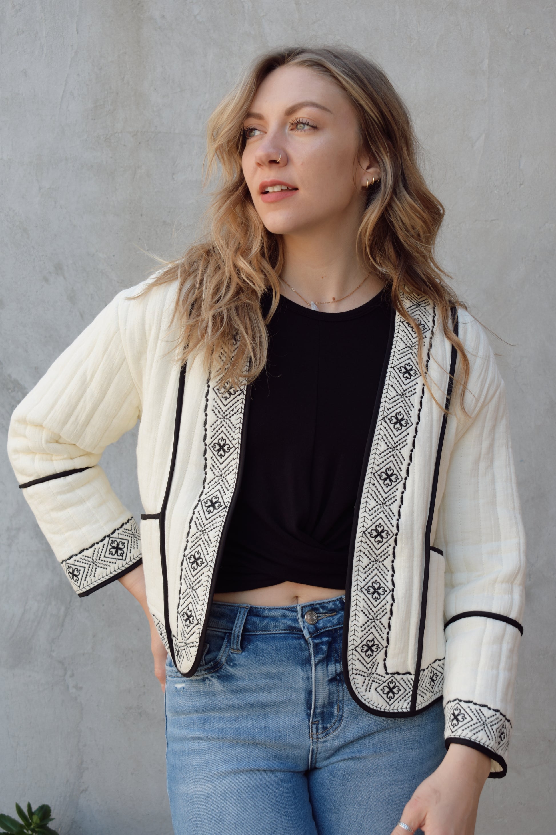 boho quilted ivory jacket with black exposed seam detailing and design along hem, has pockets, 2 clasp enclosure