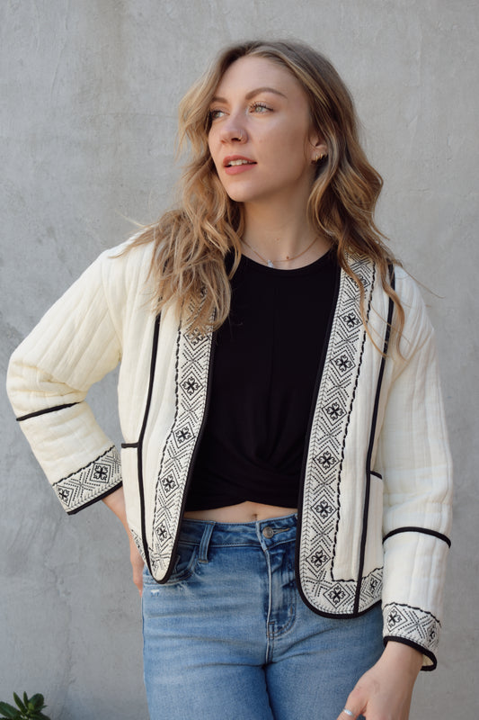 boho quilted ivory jacket with black exposed seam detailing and design along hem, has pockets, 2 clasp enclosure