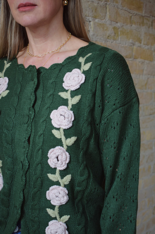 green cable knit cardigan with scalloped neckline, light pink flower crochet detailing along front ribbed cuffs and hem, hip length, relaxed fit