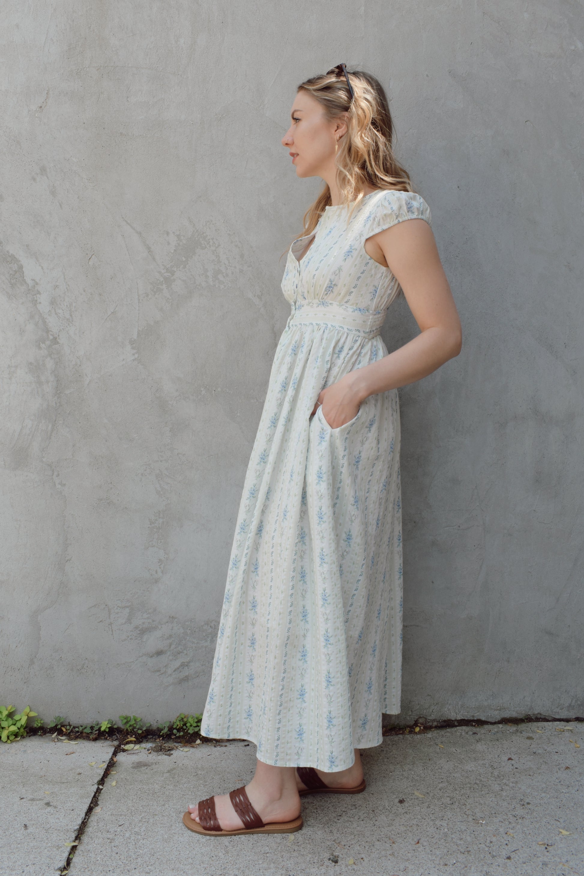 cap sleeve midi dress with ditsy floral pattern and blue buttons down the front until hitting a slit in front hem, fitted waist with smocked band in back, v neck, twirly