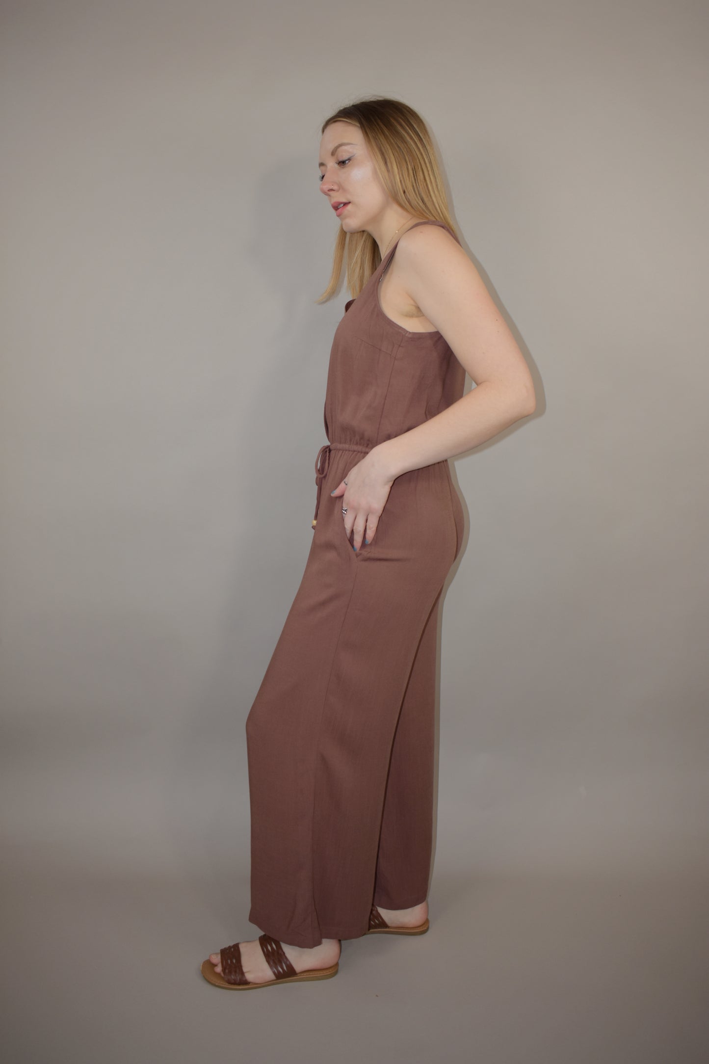 v neck jumpsuit with thin elastic waistband and drawstring with wooden bead at the end has pockets wide leg and buttons down the front of bodice