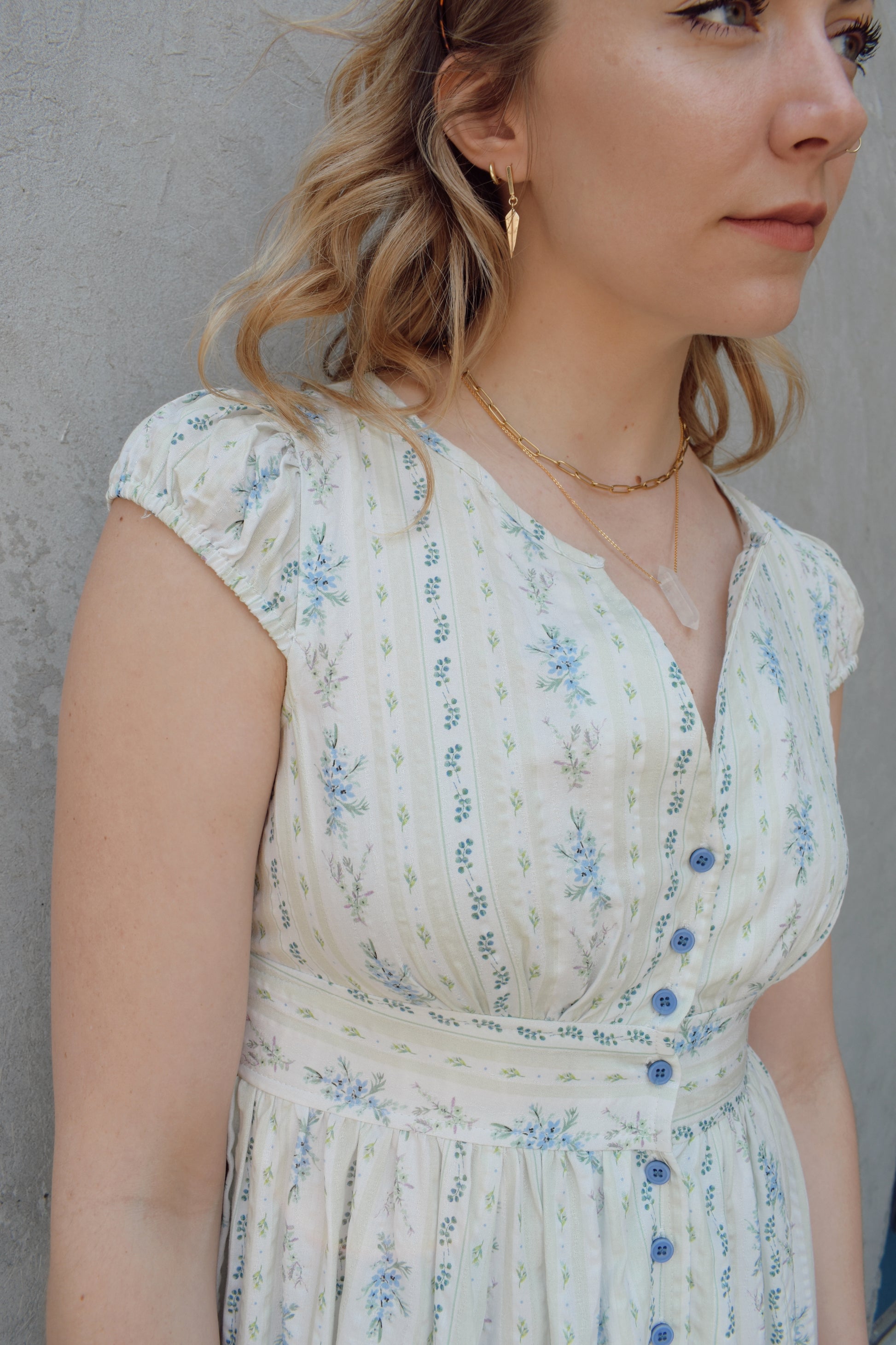 cap sleeve midi dress with ditsy floral pattern and blue buttons down the front until hitting a slit in front hem, fitted waist with smocked band in back, v neck, twirly