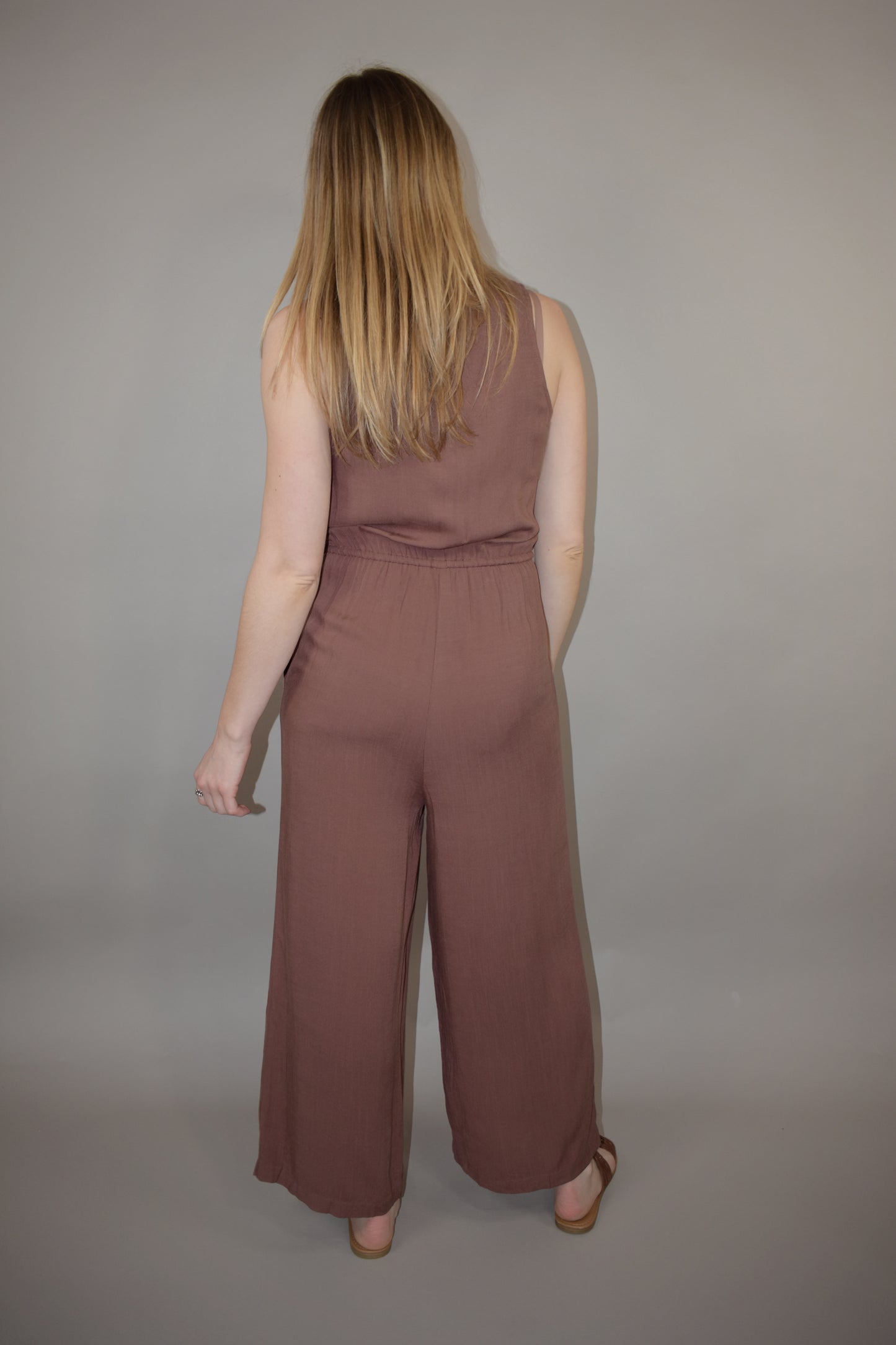 v neck jumpsuit with thin elastic waistband and drawstring with wooden bead at the end has pockets wide leg and buttons down the front of bodice