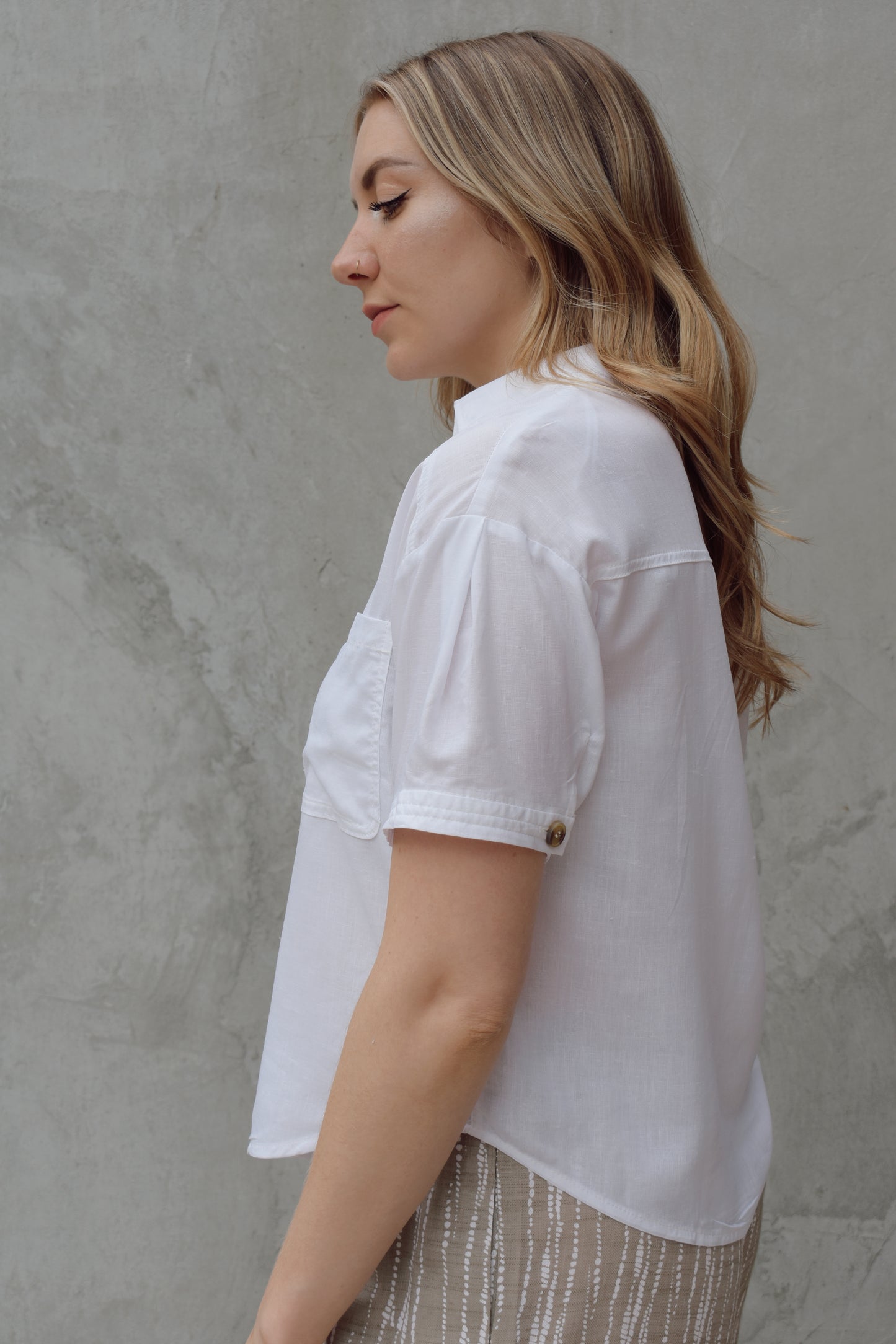 white linen button down, short sleeve, v neck with collar, 3 brown buttons, patch breast pockets, scoop hemline, button detail on back of sleeve cuff