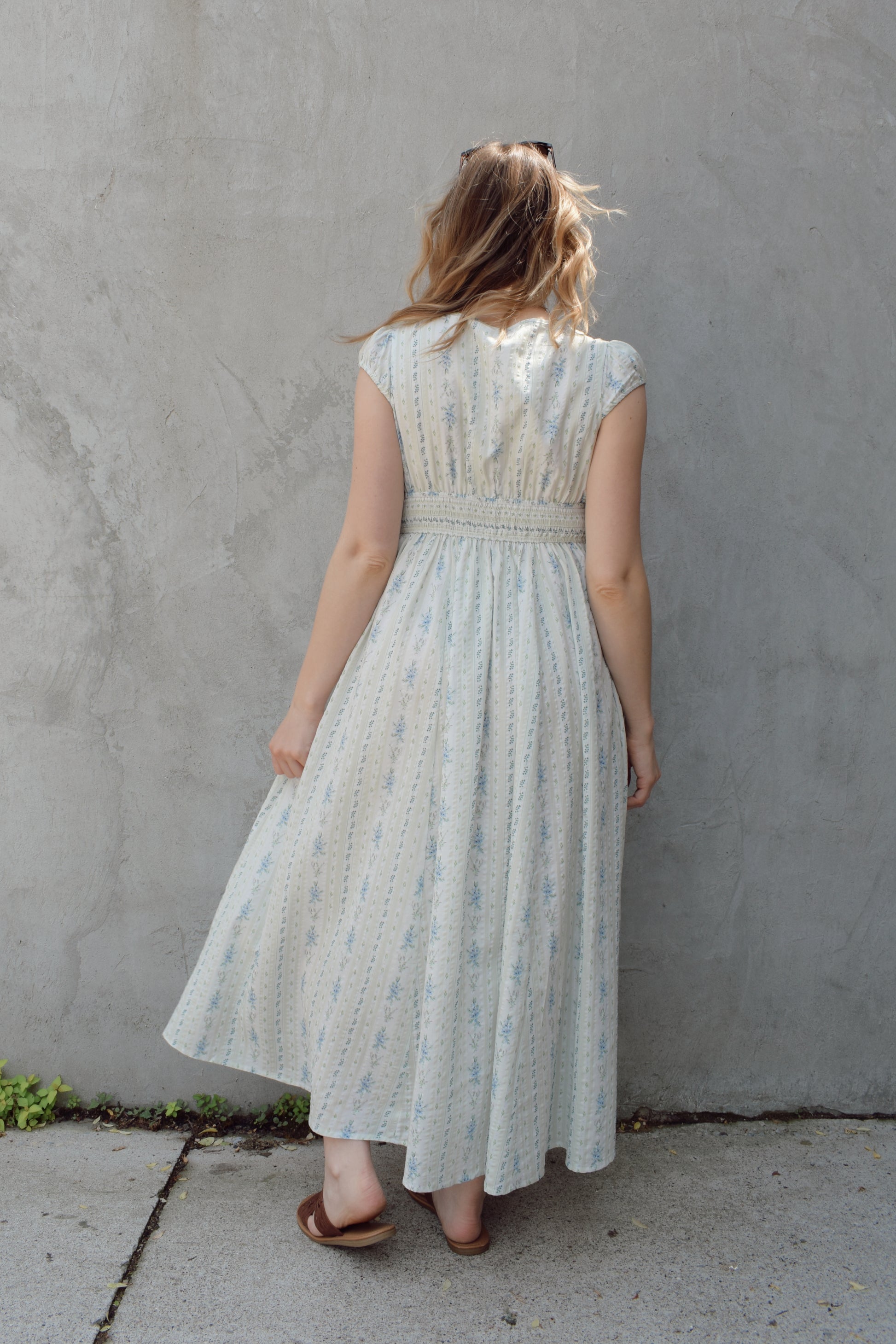 cap sleeve midi dress with ditsy floral pattern and blue buttons down the front until hitting a slit in front hem, fitted waist with smocked band in back, v neck, twirly