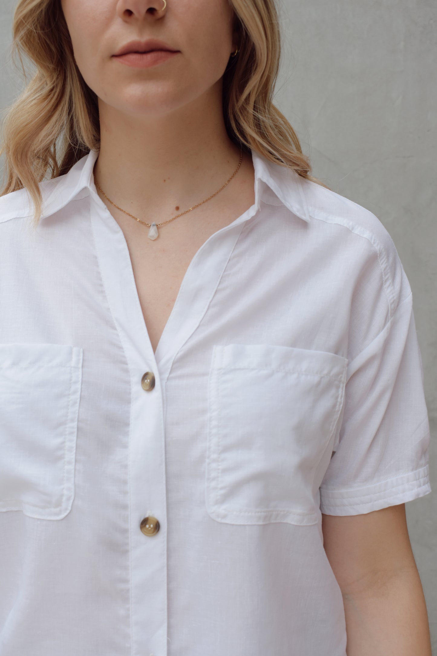 white linen button down, short sleeve, v neck with collar, 3 brown buttons, patch breast pockets, scoop hemline, button detail on back of sleeve cuff