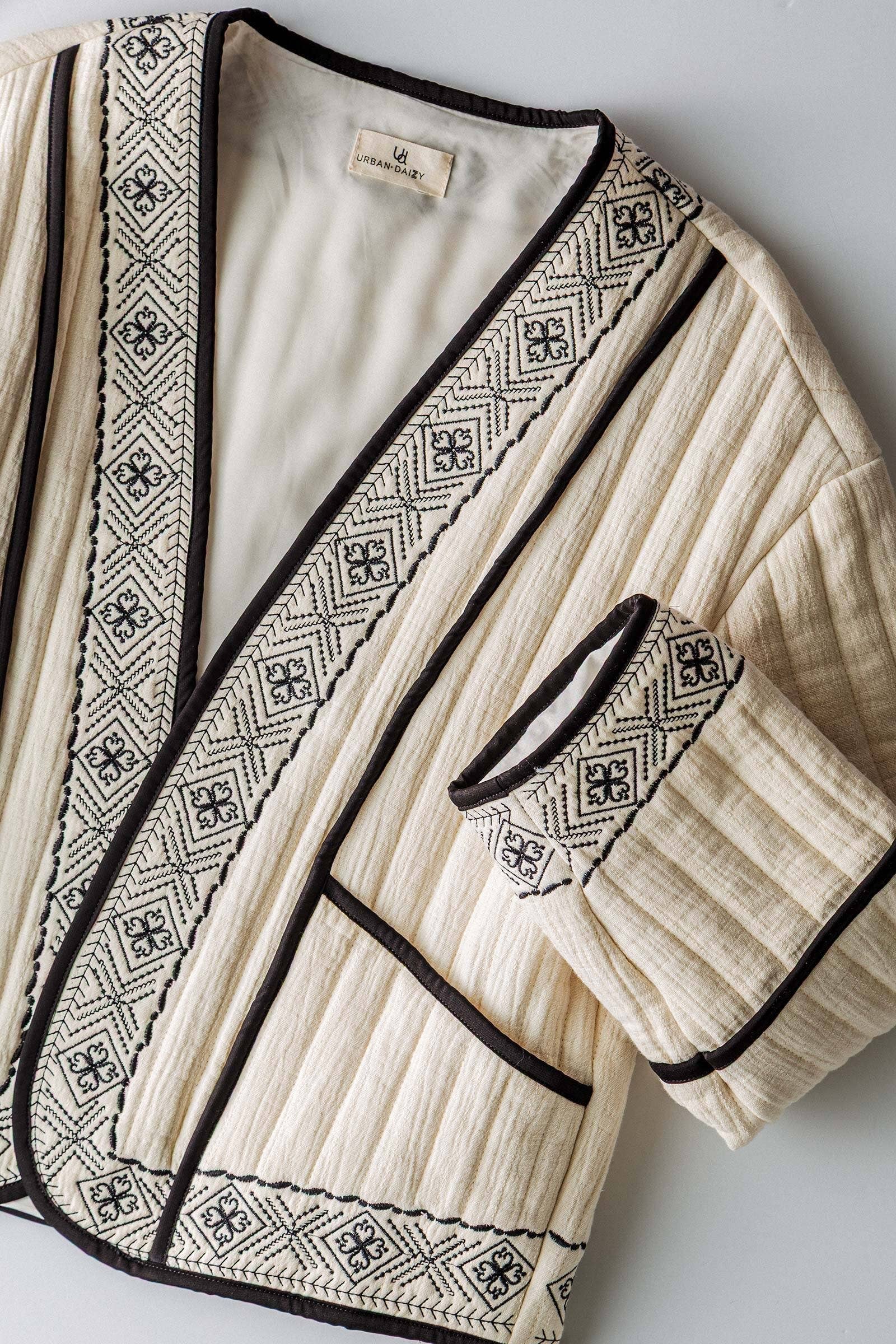 boho quilted ivory jacket with black exposed seam detailing and design along hem, has pockets, 2 clasp enclosure 