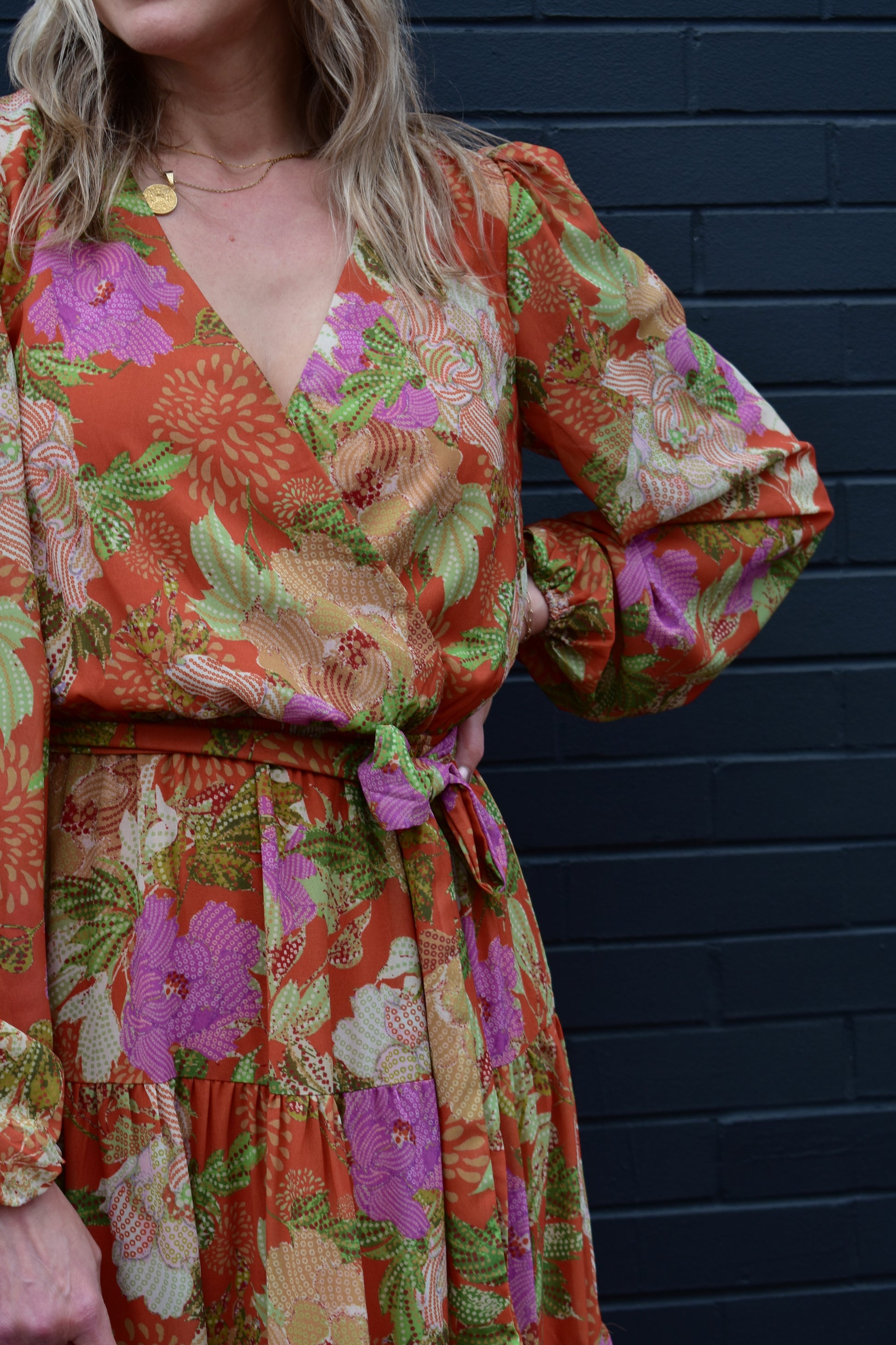 Long sleeve midi dress with floral print. Colors are an orange background with yellow, purple, light pink, green, white and cream. Wrap V neckline, lightweight fabric with lining, elastic at wrists, wrap at waist, tiered skirt. 