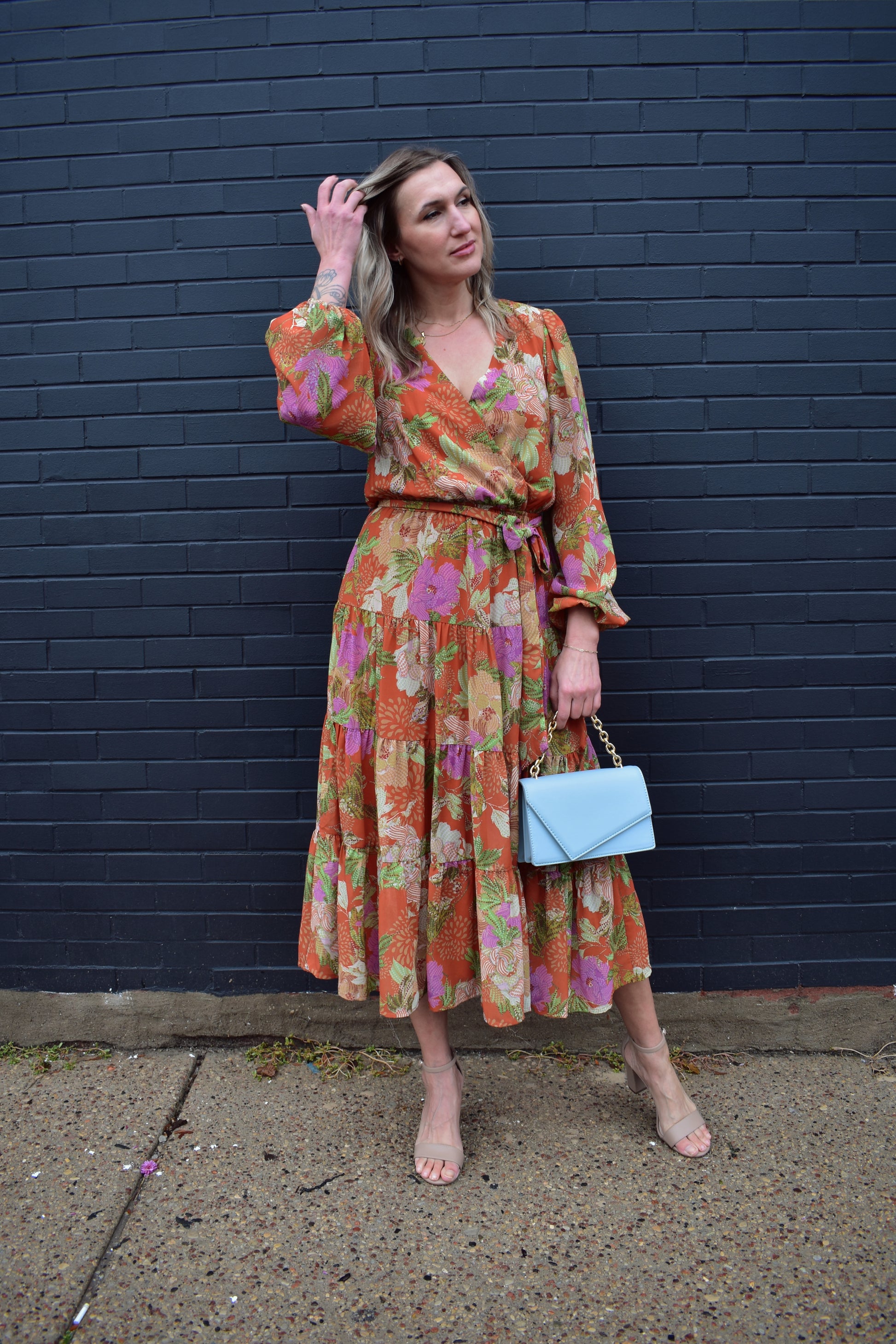 Long sleeve midi dress with floral print. Colors are an orange background with yellow, purple, light pink, green, white and cream. Wrap V neckline, lightweight fabric with lining, elastic at wrists, wrap at waist, tiered skirt. 