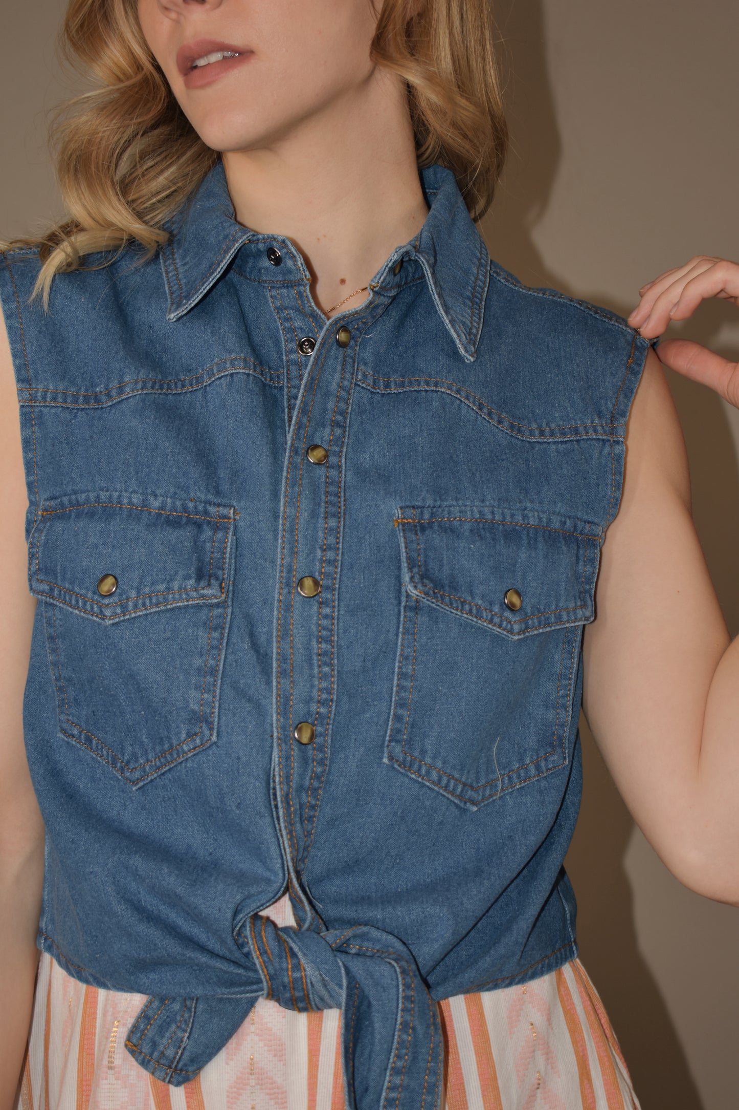 sleeveless western style denim button down shirt with tie in front at hem. two breast pockets with button enclosure. medium wash.