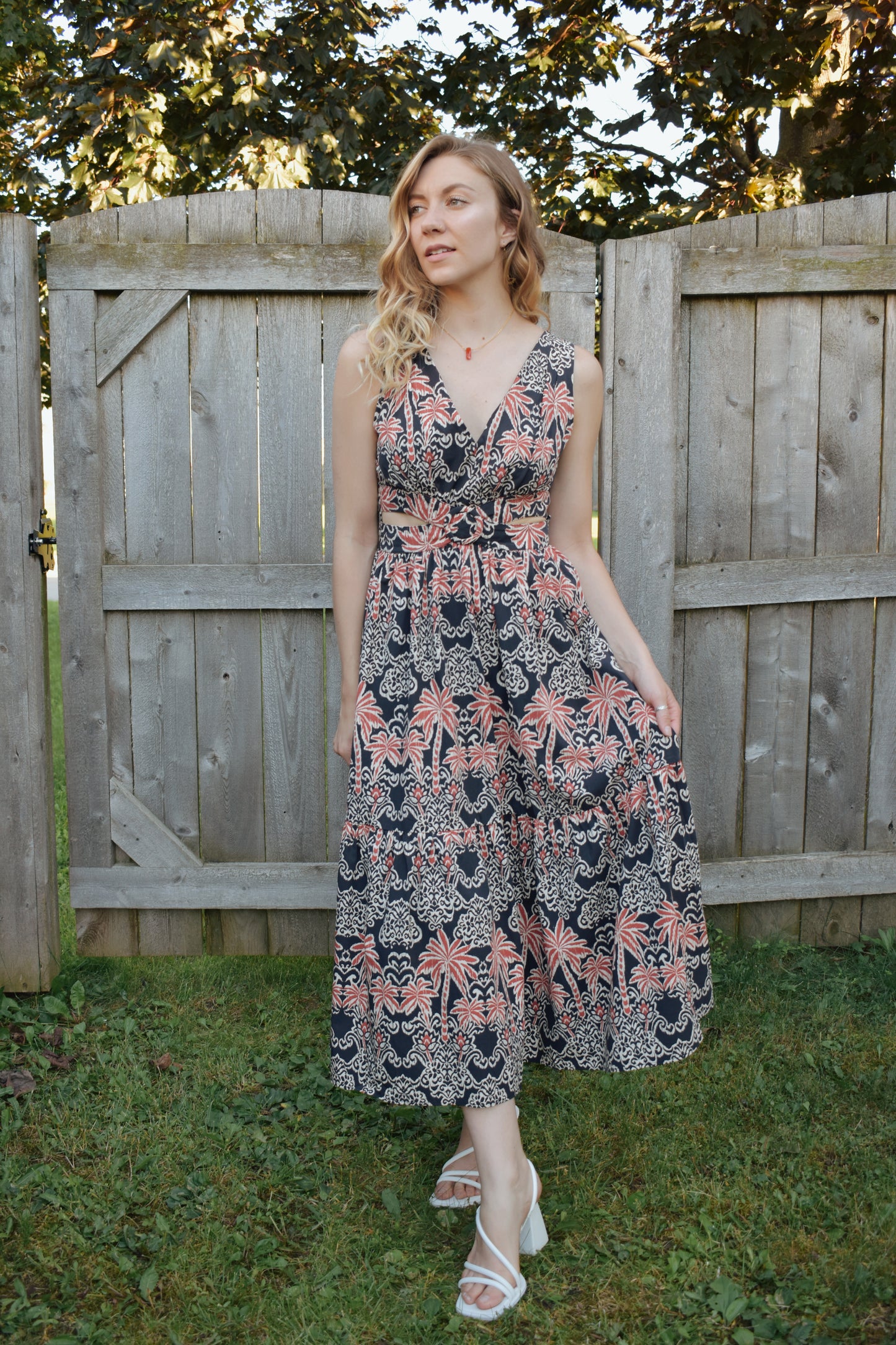 v neck midi dress with oval cut outs at waistline with circle loop in the center. square neck on back with tie across the top. sleeveless with thick tank straps. dark blue background with white and light red summer print. smocked on back waistline for stretch.