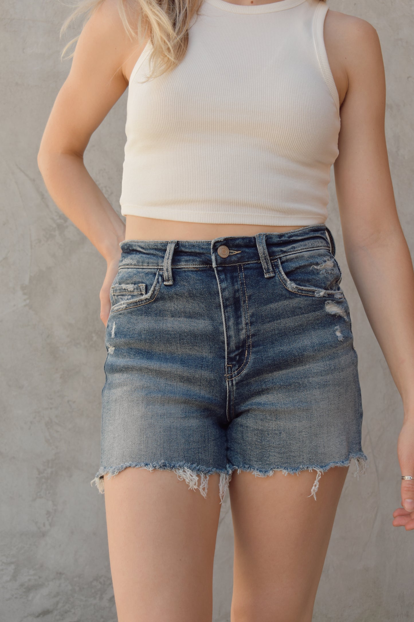 high rise stretch denim shorts with distressing marks and raw frayed hem medium wash