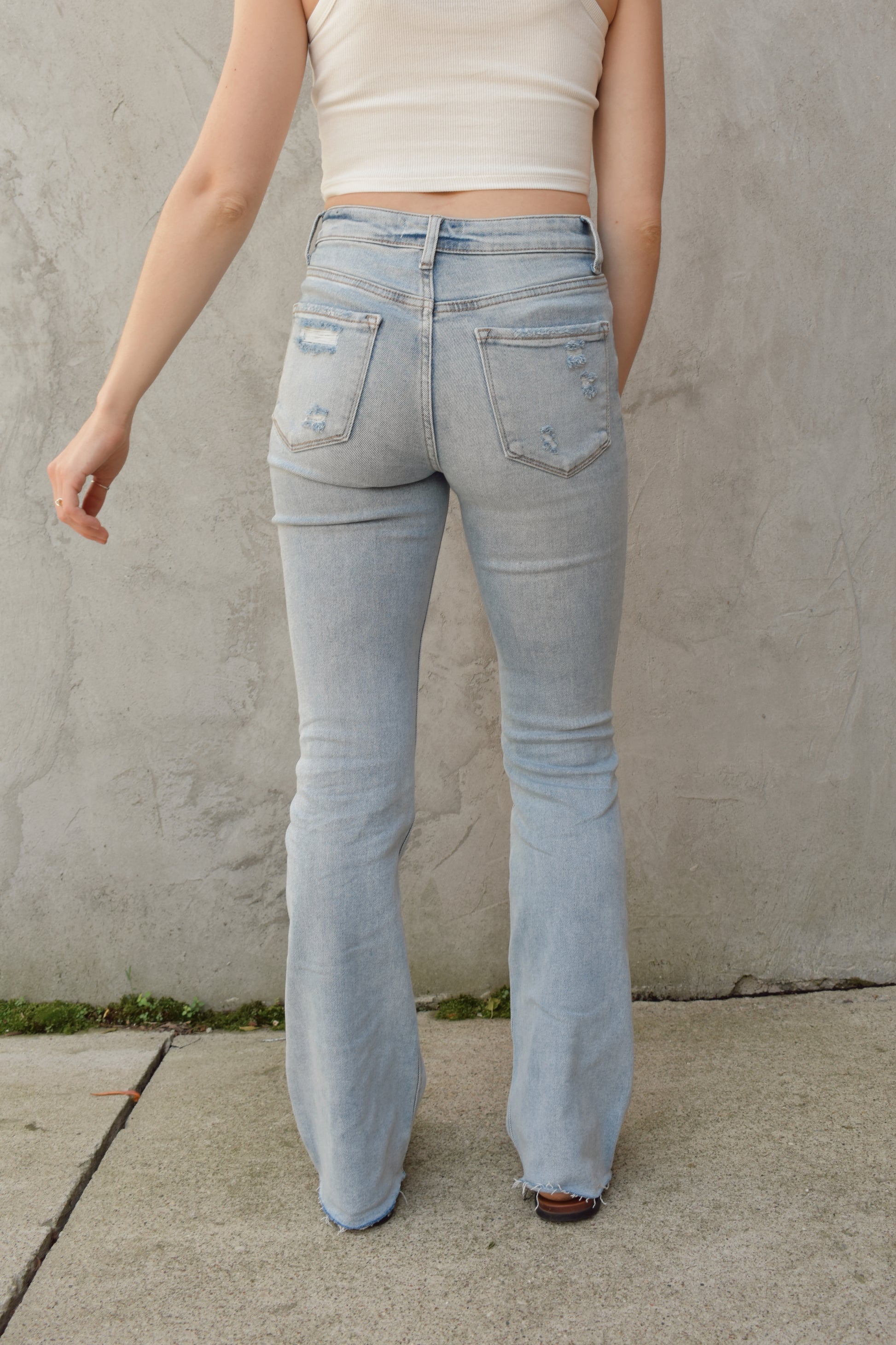 full length high rise bootcut jeans light wash with hole in right knee and slight distressing on other leg raw hem stretch denim distressing on back pockets