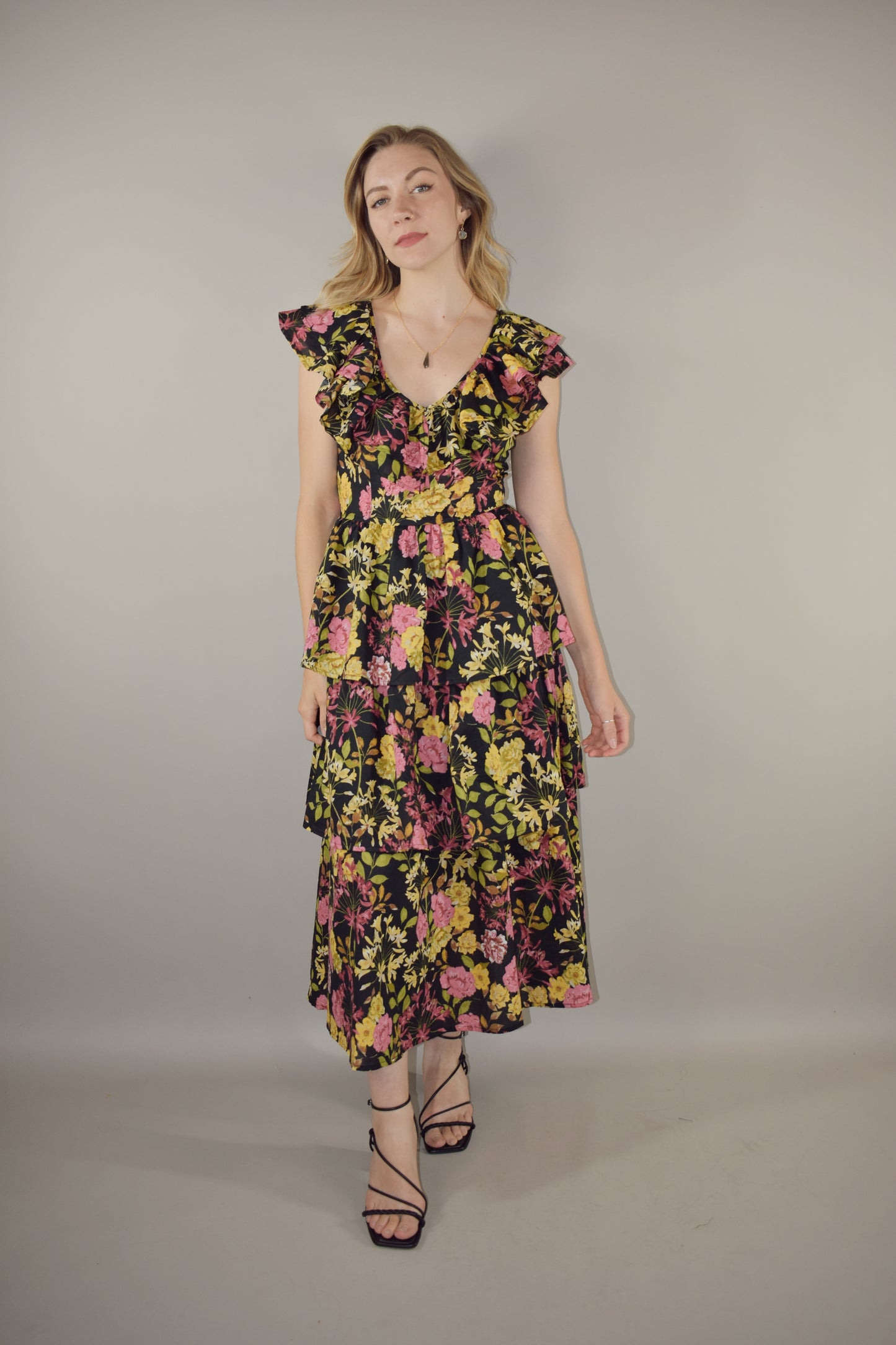 midi tiered floral dress with black background and pink, yellow, green and neutral tones in the floral pattern. v neck with cap flutter sleeves that are also layered. fitted bodice and invisible back zip enclosure. 