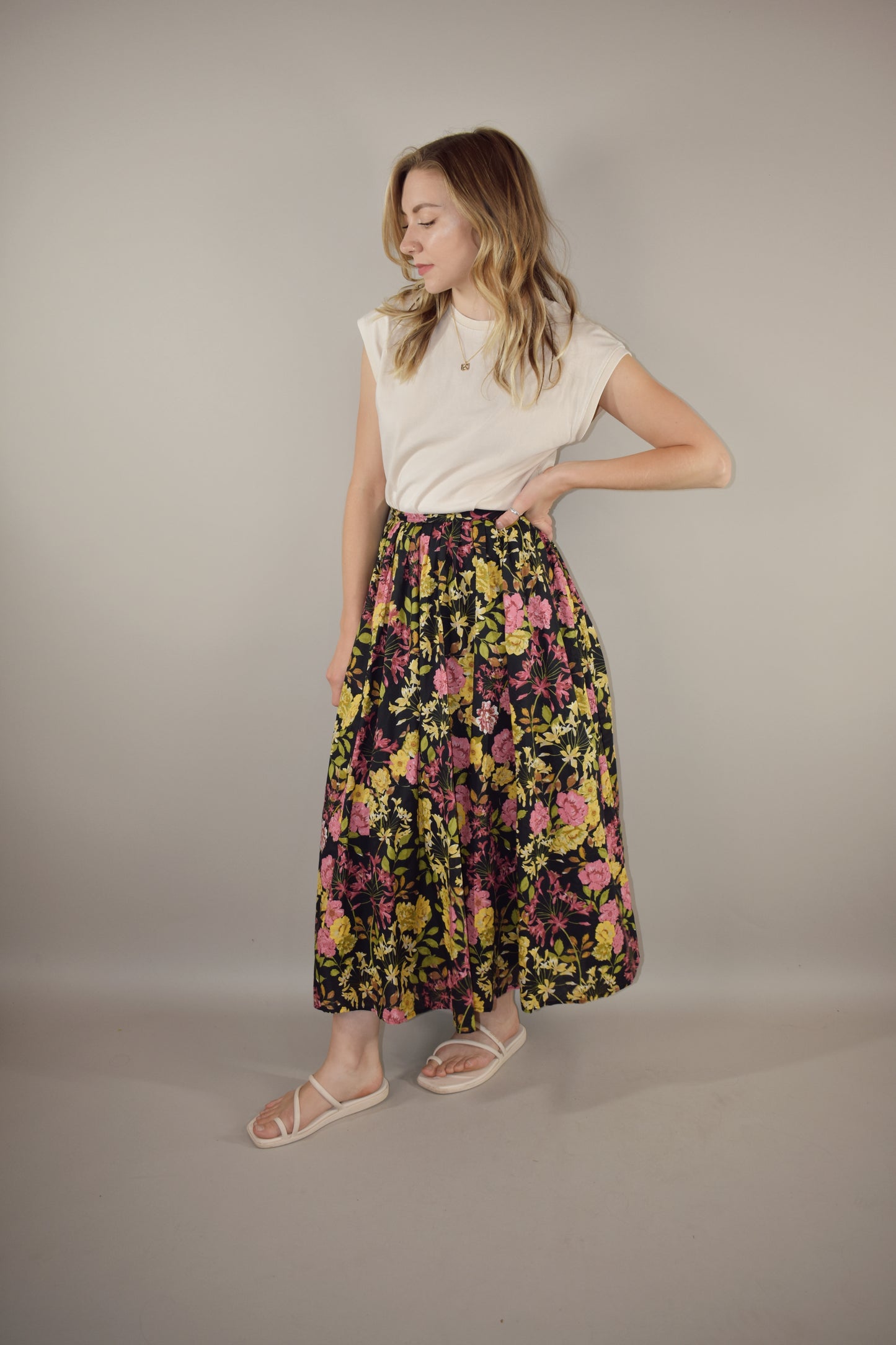 pink, yellow, green and neutral tone floral print on a black background. flowy lined midi skirt with side zip enclosure. fitted waist with no elastic. 