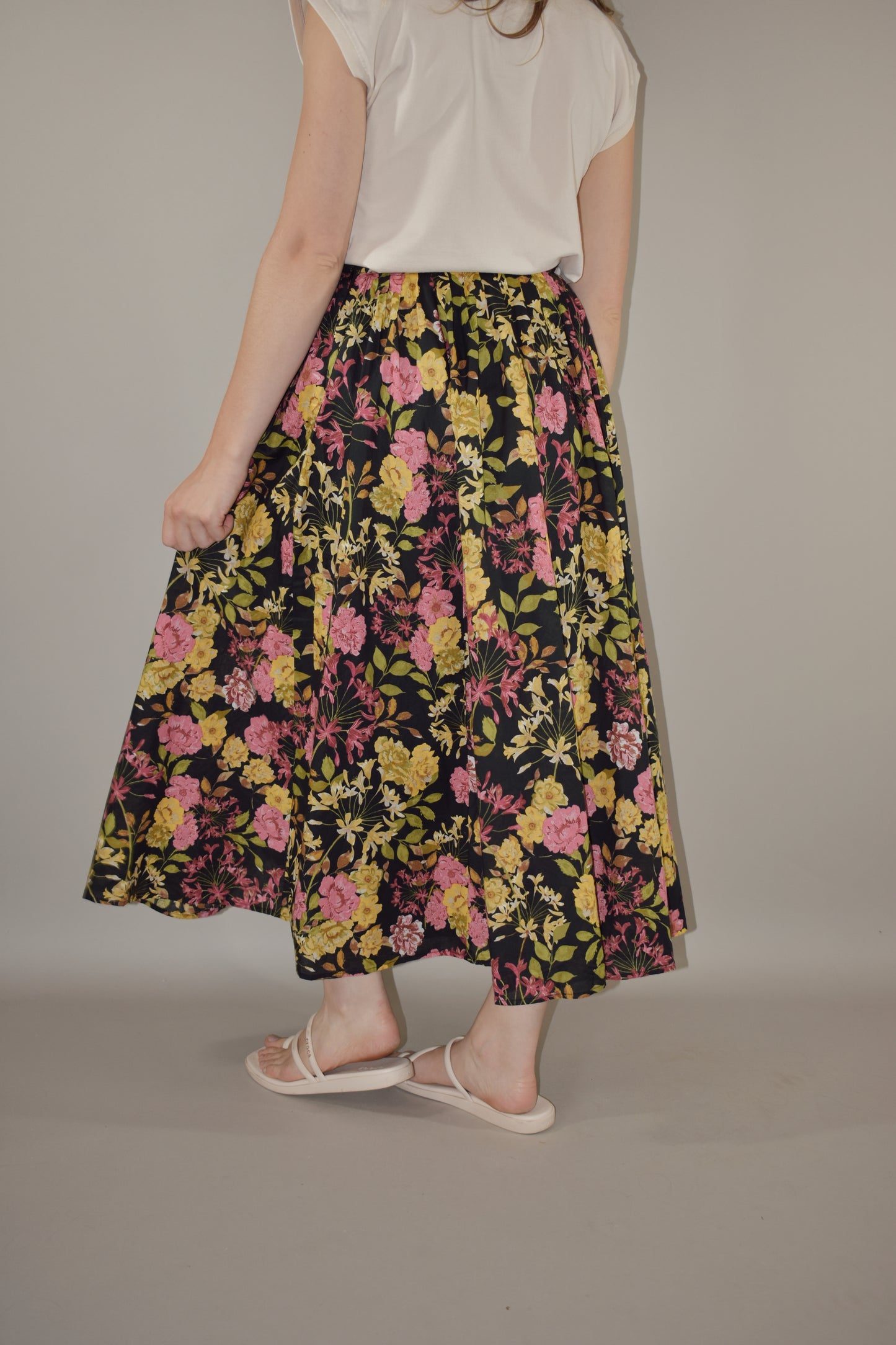 pink, yellow, green and neutral tone floral print on a black background. flowy lined midi skirt with side zip enclosure. fitted waist with no elastic. 