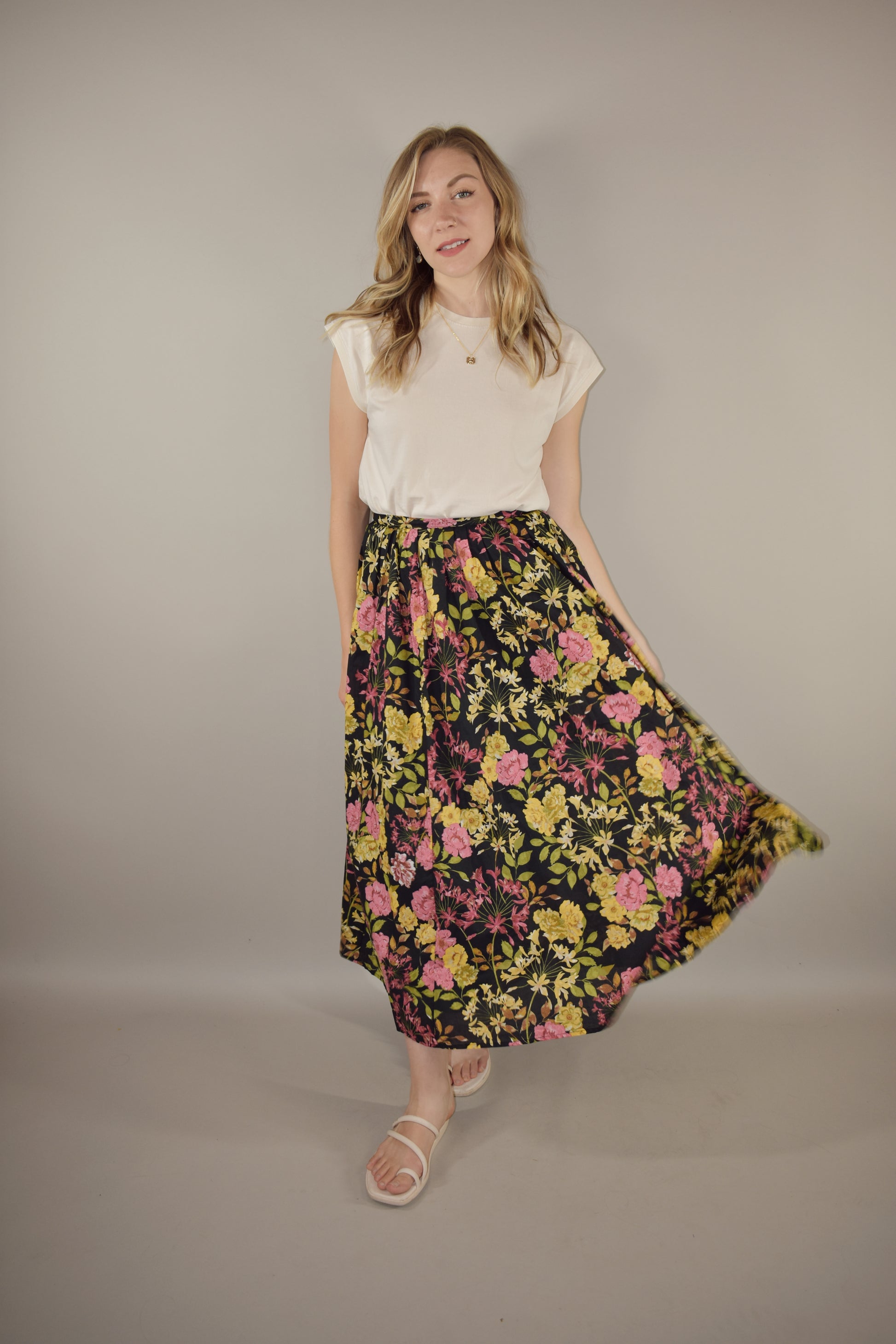 pink, yellow, green and neutral tone floral print on a black background. flowy lined midi skirt with side zip enclosure. fitted waist with no elastic. 