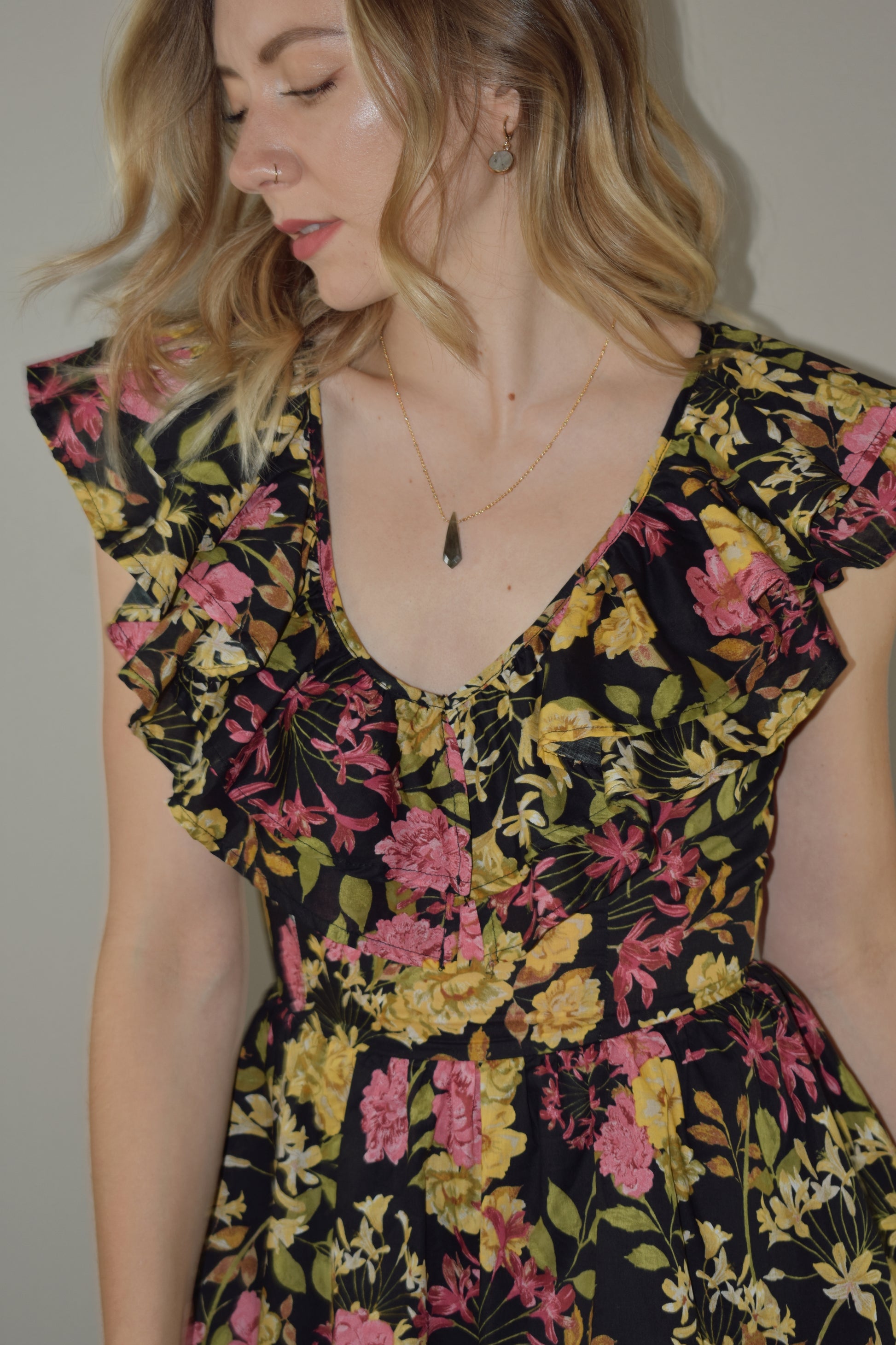 midi tiered floral dress with black background and pink, yellow, green and neutral tones in the floral pattern. v neck with cap flutter sleeves that are also layered. fitted bodice and invisible back zip enclosure. 