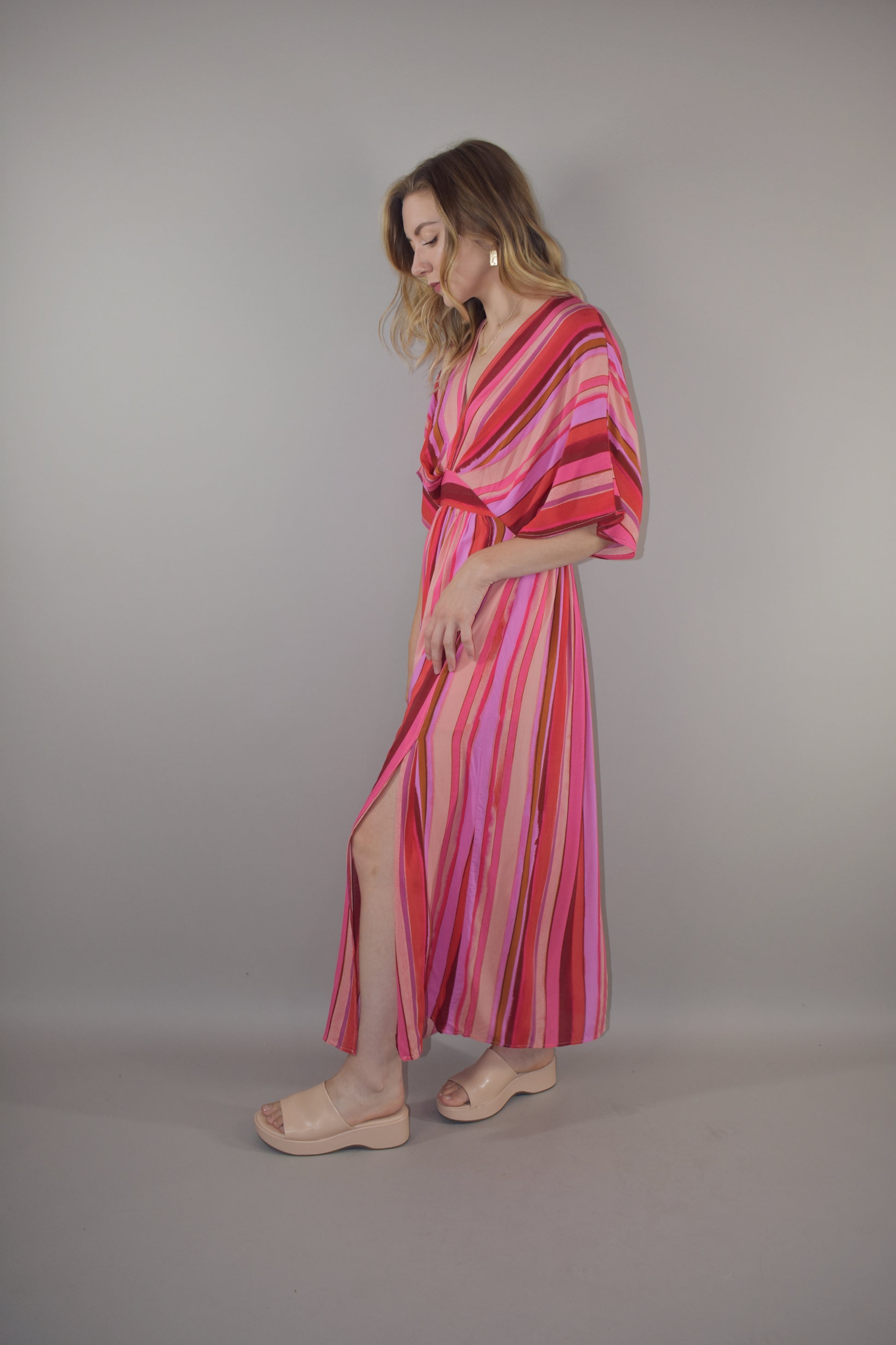 tones of red vertical striped maxi dress with flowy lightweight fabric, lined with a synched stretchy waistband and deep v neck with a hook and eye enclosure and dolman sleeves that hit at the elbow. side slits that are semi hidden unless walking. button enclosure at back neckline