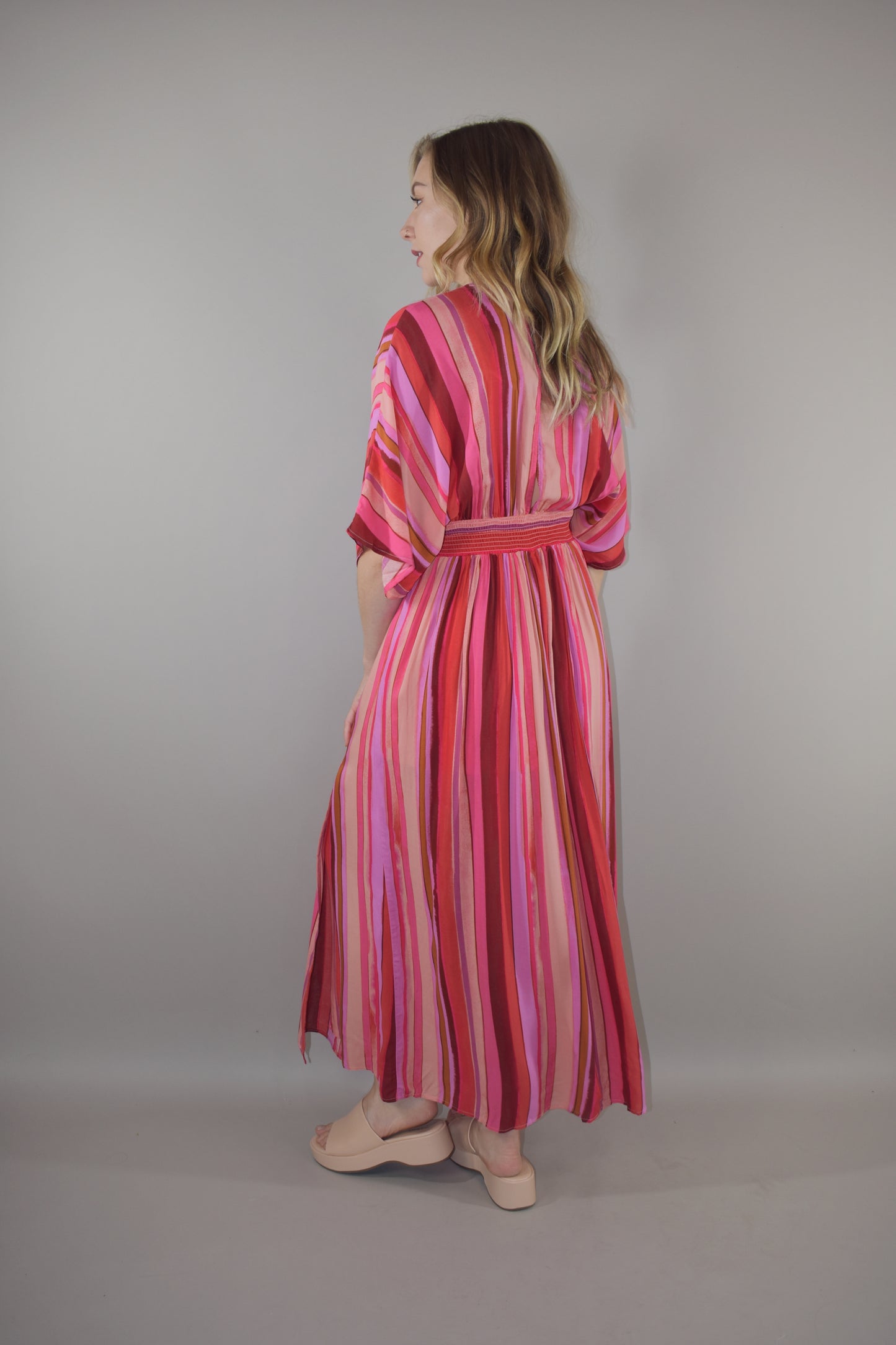 tones of red vertical striped maxi dress with flowy lightweight fabric, lined with a synched stretchy waistband and deep v neck with a hook and eye enclosure and dolman sleeves that hit at the elbow. side slits that are semi hidden unless walking. button enclosure at back neckline