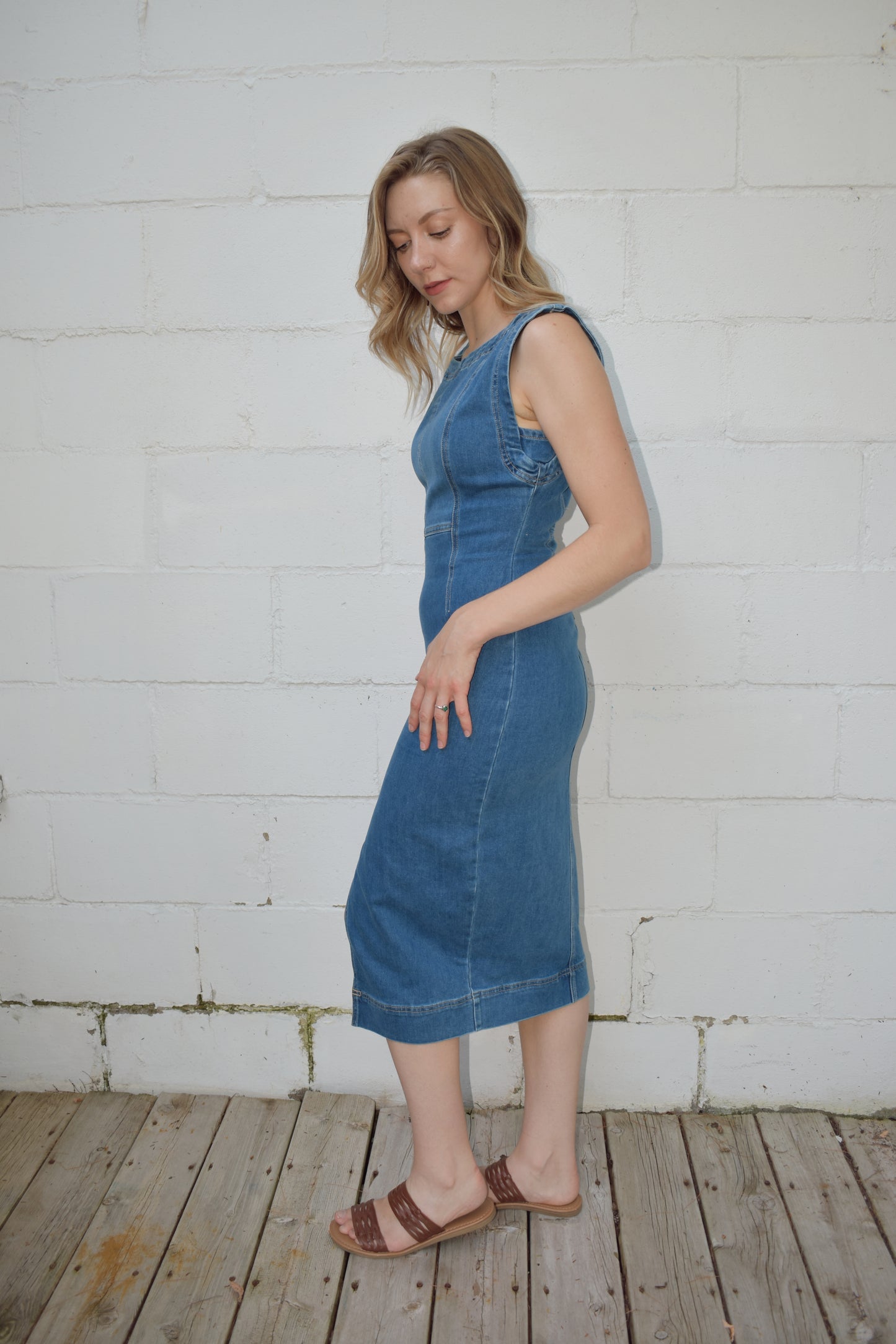 fitted midi length medium wash denim stretch dress. high scoop neck with zip back enclosure. seam detailing on bodice. slit up front of skirt.