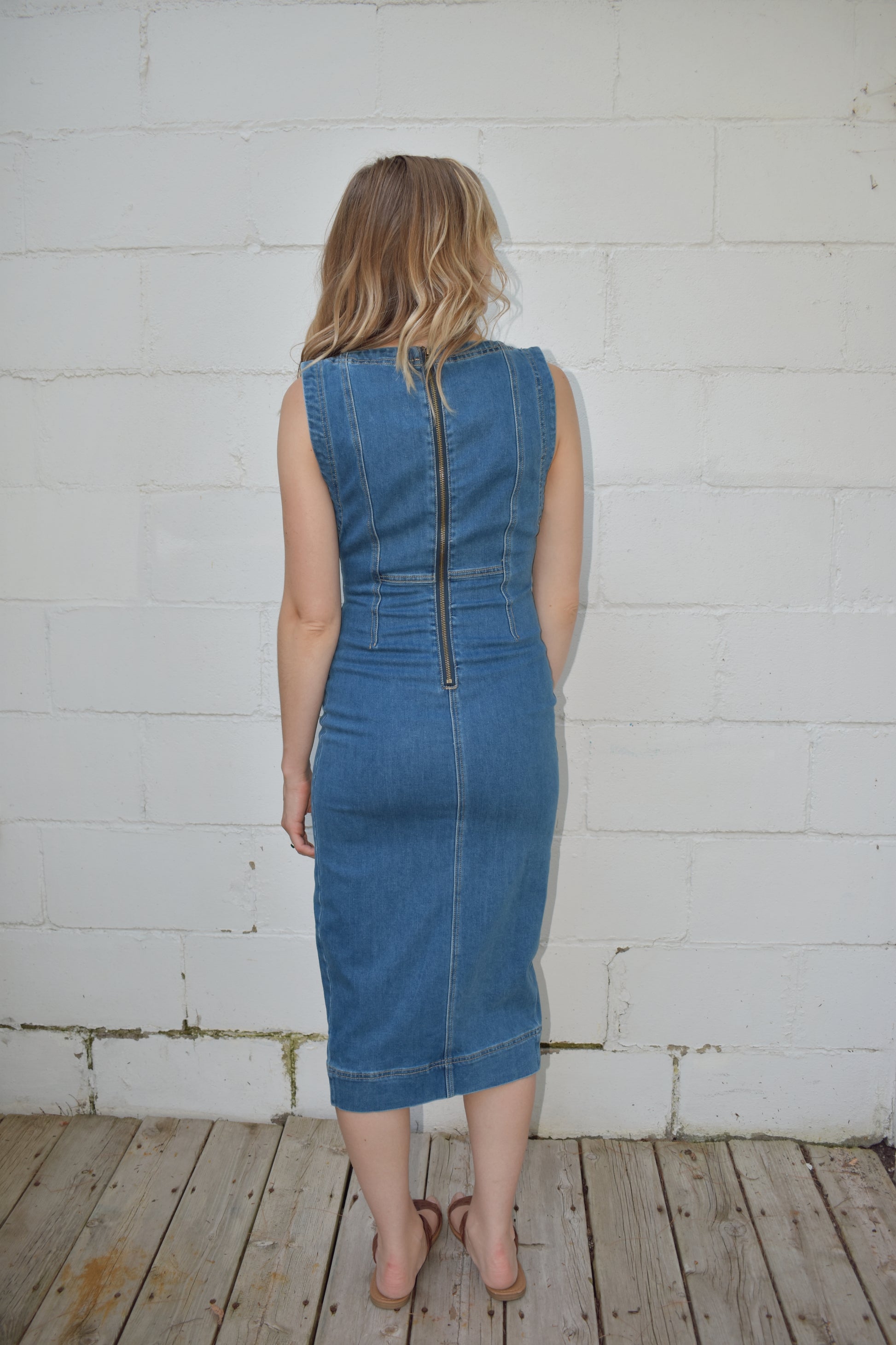 fitted midi length medium wash denim stretch dress. high scoop neck with zip back enclosure. seam detailing on bodice. slit up front of skirt.