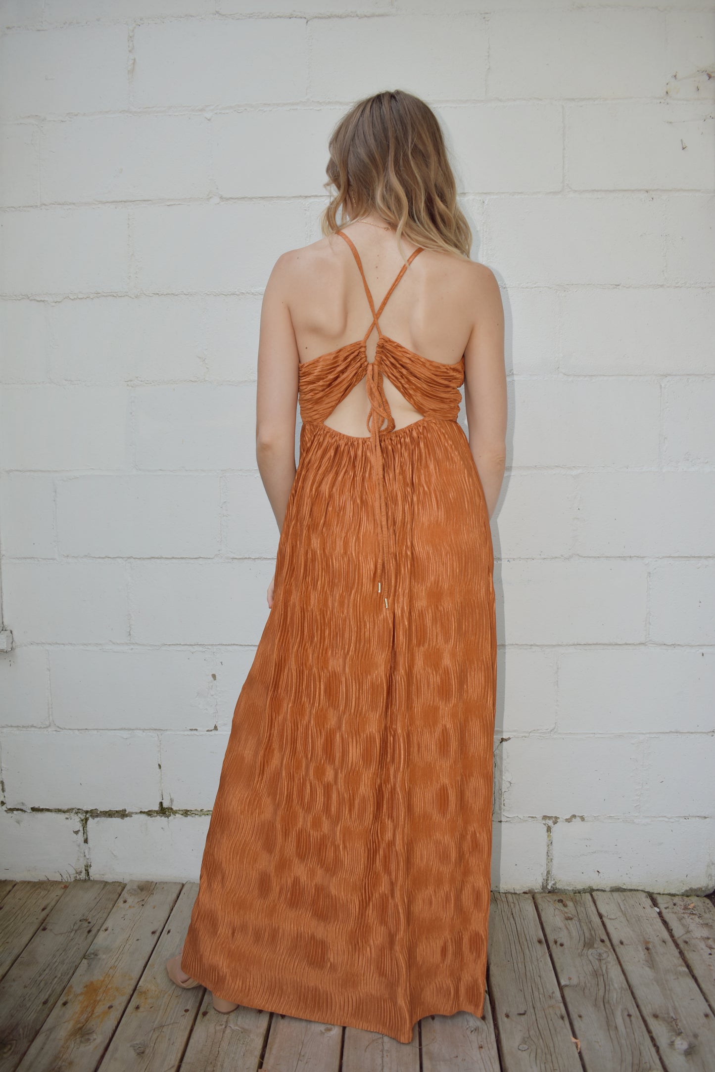 deep v neck spaghetti strap dress with a wavy texture fabric that illuminates when in the sun. maxi dress. straps cross in the back and tie which features a triangle cutout. theres a metal bar that connects the band just under the neckline.