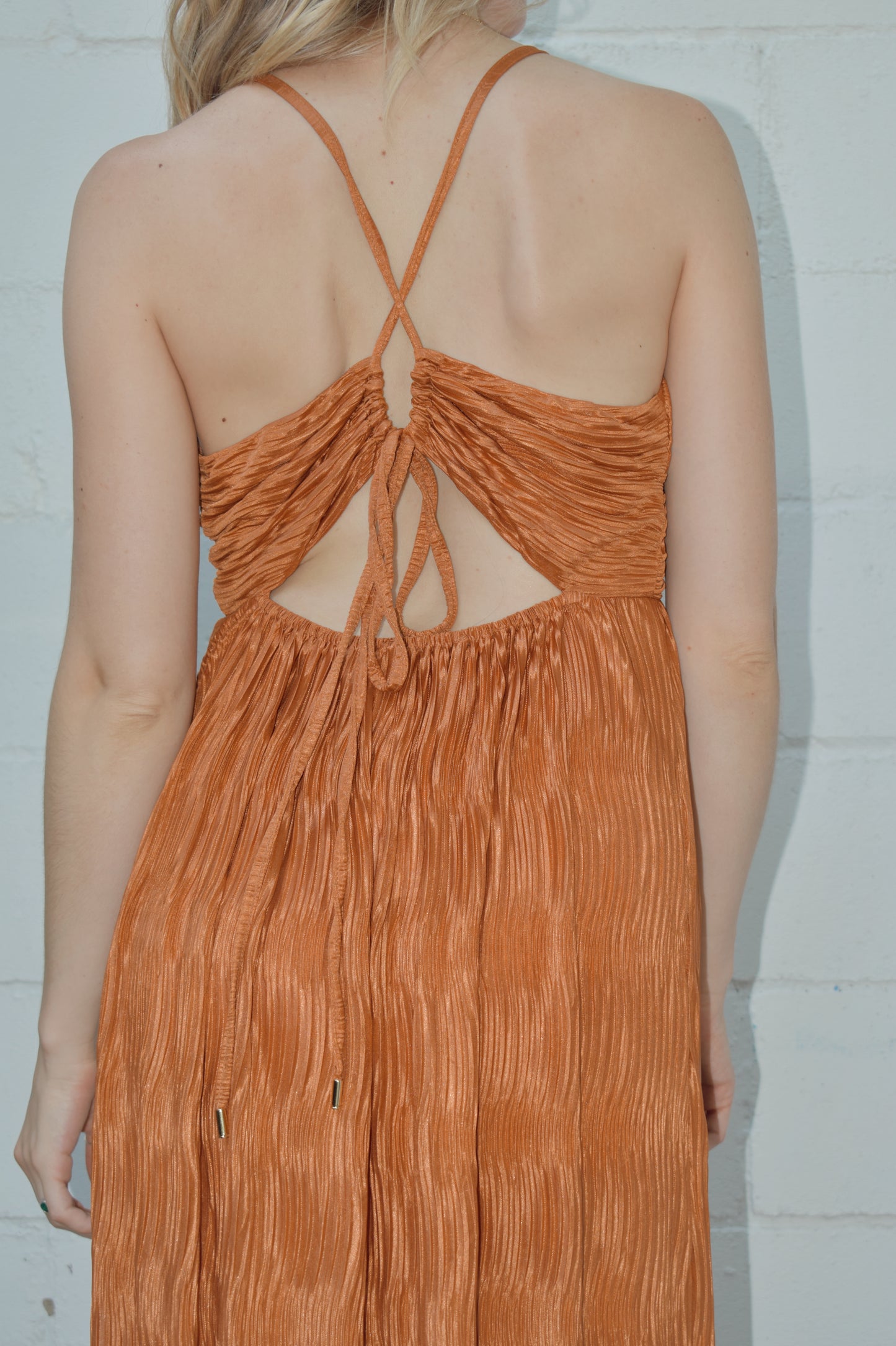 deep v neck spaghetti strap dress with a wavy texture fabric that illuminates when in the sun. maxi dress. straps cross in the back and tie which features a triangle cutout. theres a metal bar that connects the band just under the neckline.