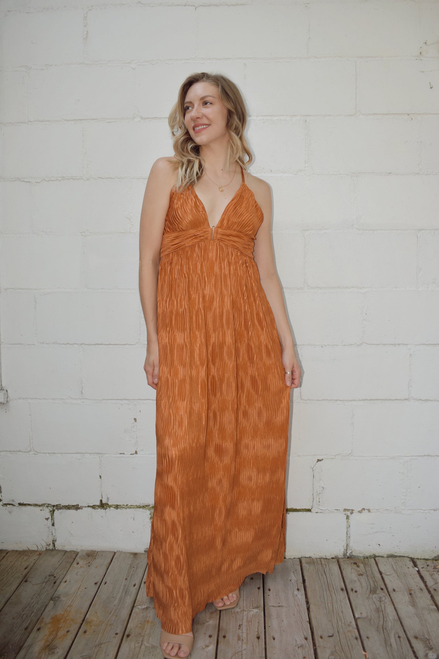 deep v neck spaghetti strap dress with a wavy texture fabric that illuminates when in the sun. maxi dress. straps cross in the back and tie which features a triangle cutout. theres a metal bar that connects the band just under the neckline.