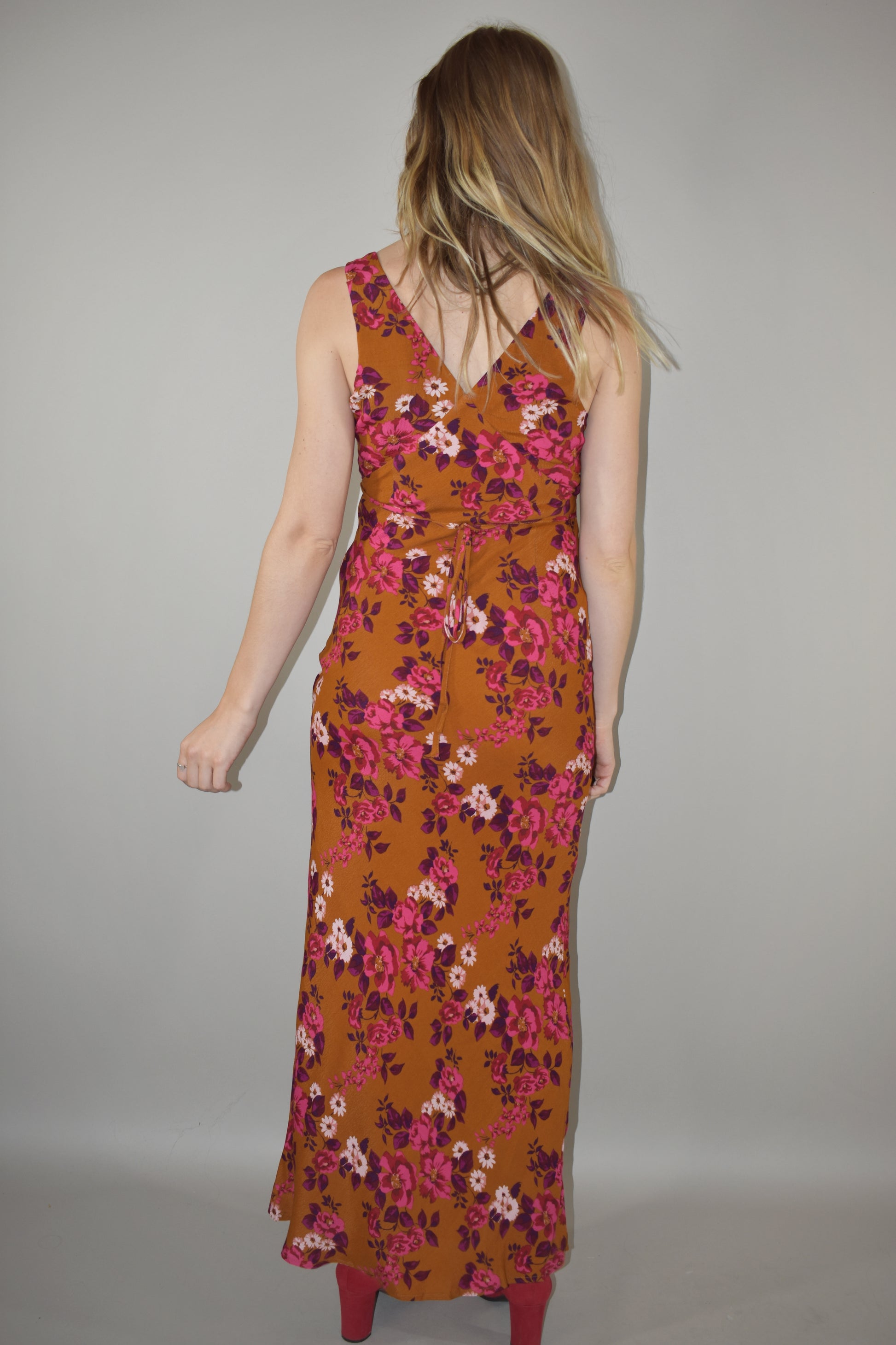 elegant floral maxi dress, v front and back neckline, more fitted through bodice and hips, skinny tie at waist that ties in the back, hidden side zip enclosure. Rust, pink, plum, fuchsia and white colors.