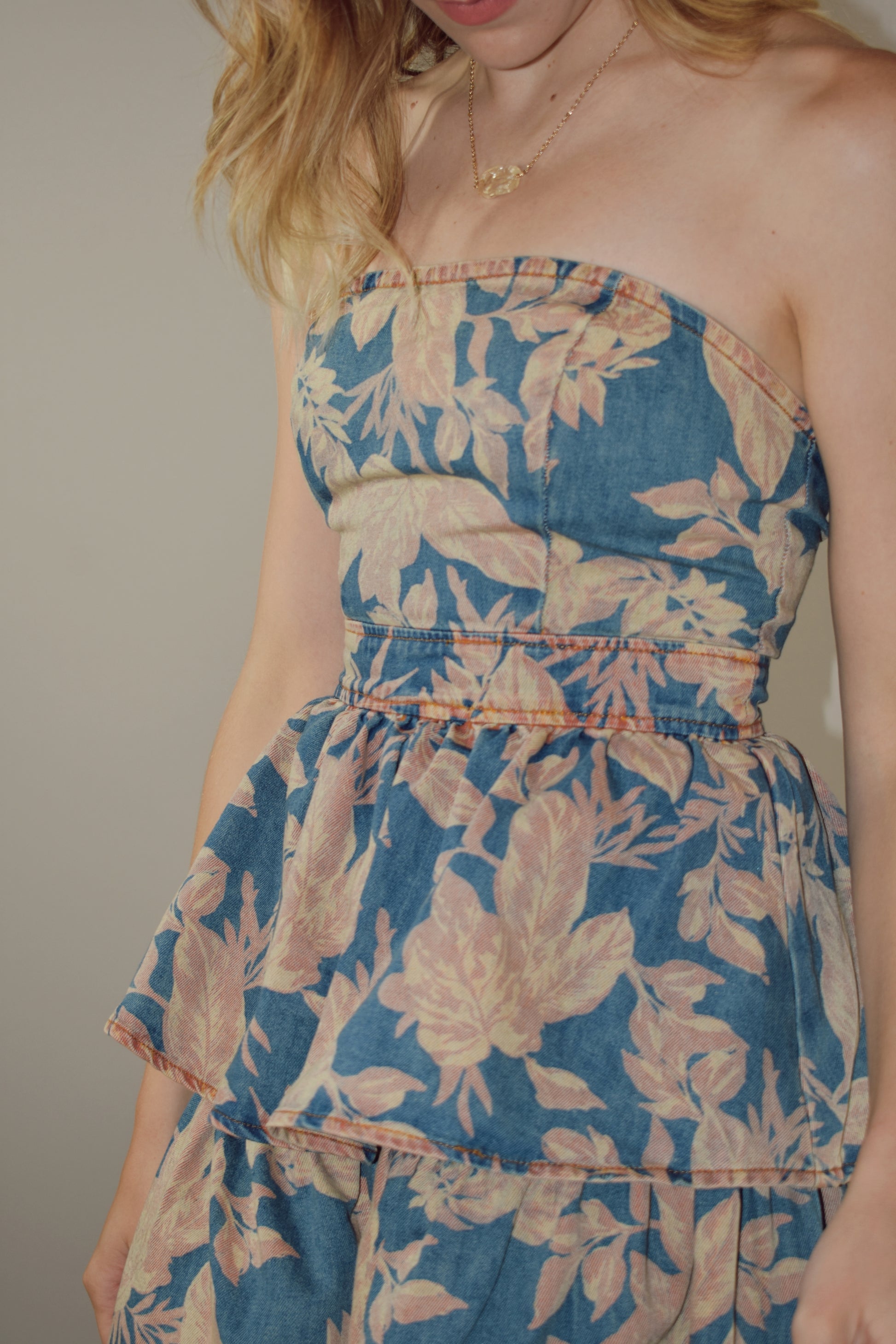 denim floral mini dress, strapless, fitted bodice, zip enclosure on back. tiered skirt, peachy tan floral pattern on light denim background.