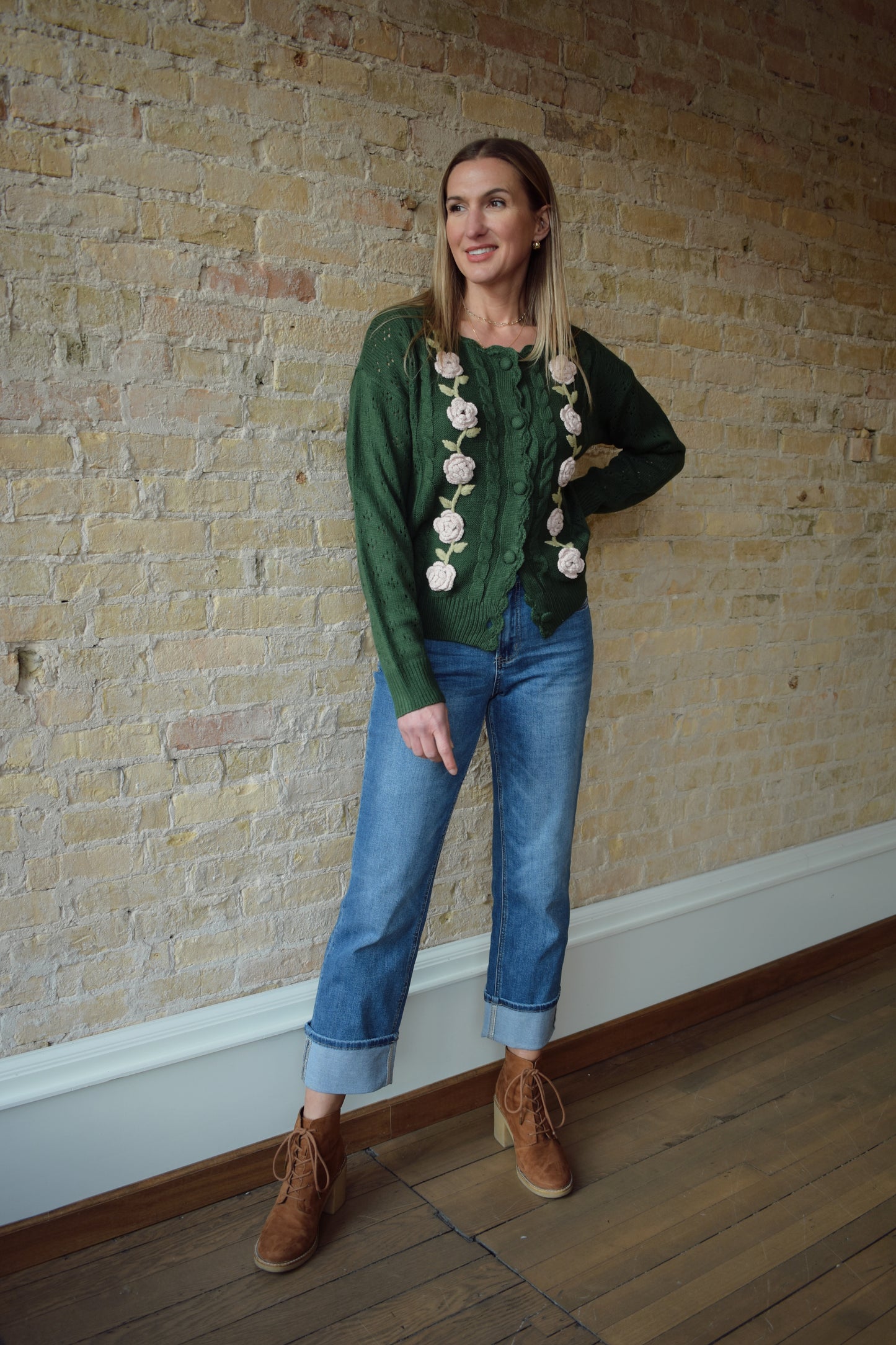 green cable knit cardigan with scalloped neckline, light pink flower crochet detailing along front ribbed cuffs and hem, hip length, relaxed fit