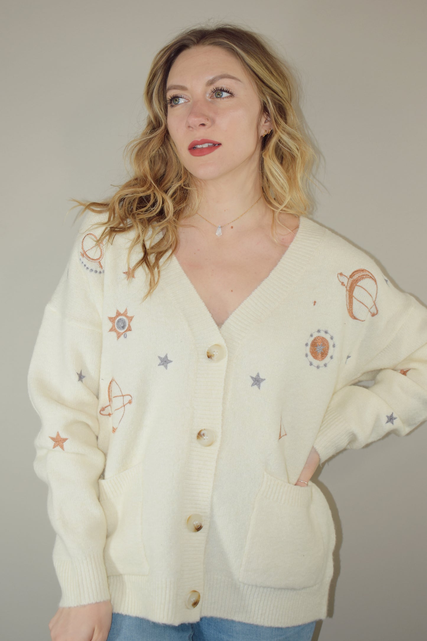 cream slouchy v neck button down cardigan hits just below hips and is embroidered with stars moons and suns has front patch pockets and drop shoulders