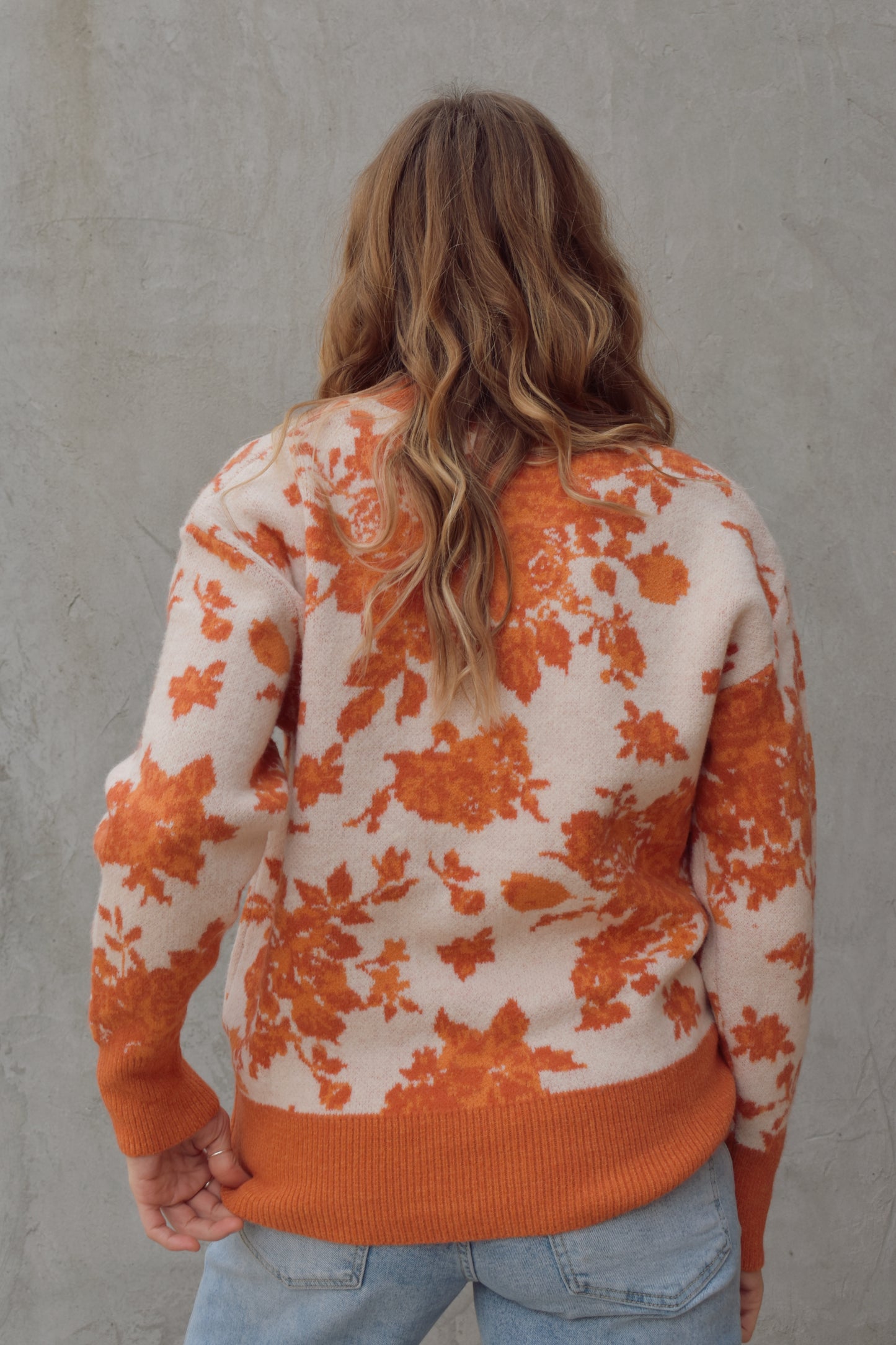 ivory and shades of orange high neck sweater with a leafy floral design. hemline neckline and cuffs are solid orange and ribbed. full length, relaxed fit, drop shoulder.