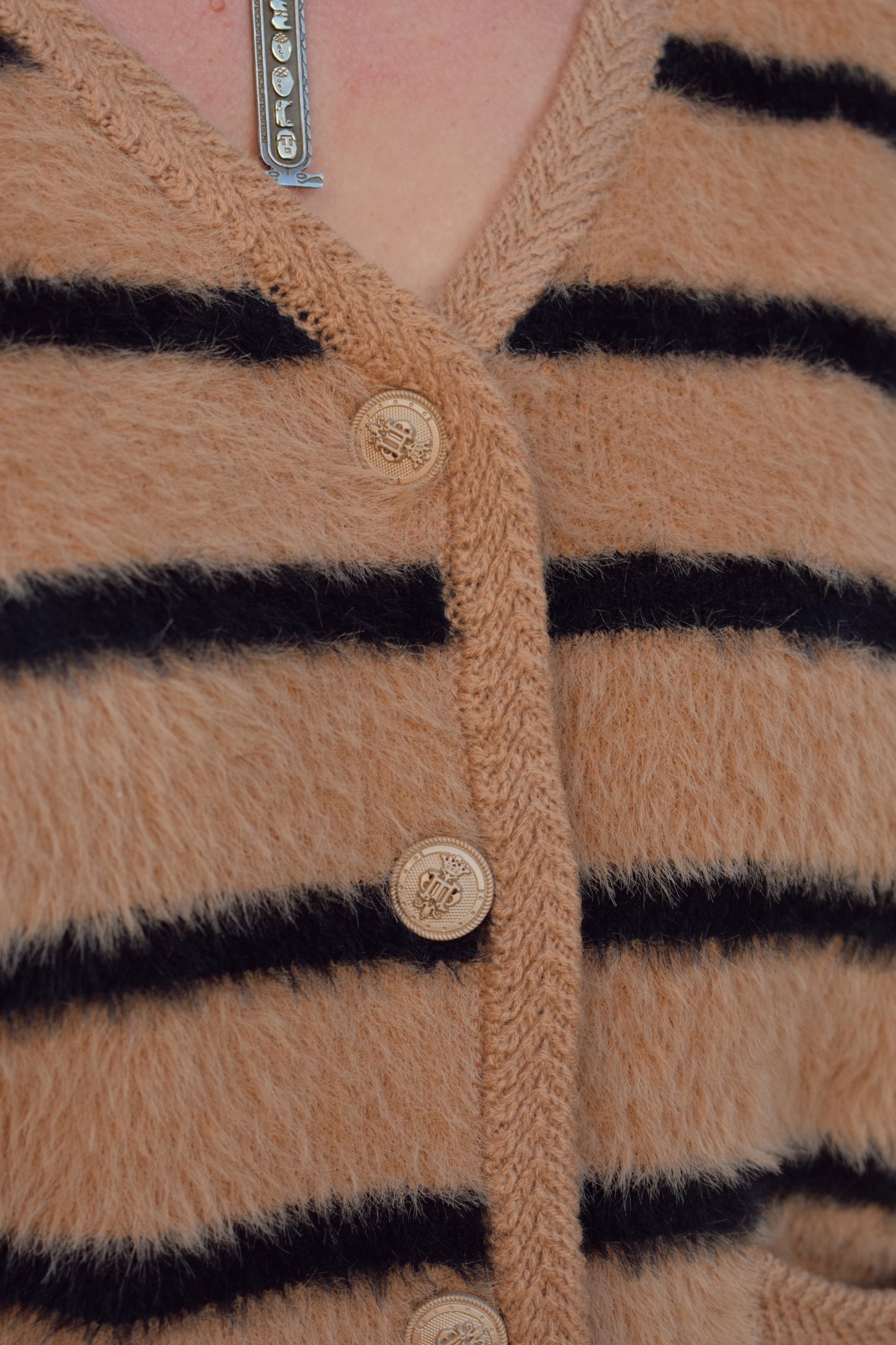 light brown mohair v neck button down cardigan with light brown sailor buttons and black horizontal stripes. two pockets on front that open at the top. outlined with a braided texture on neck line and down the front and on edge of pockets. drop shoulders, slightly cropped.