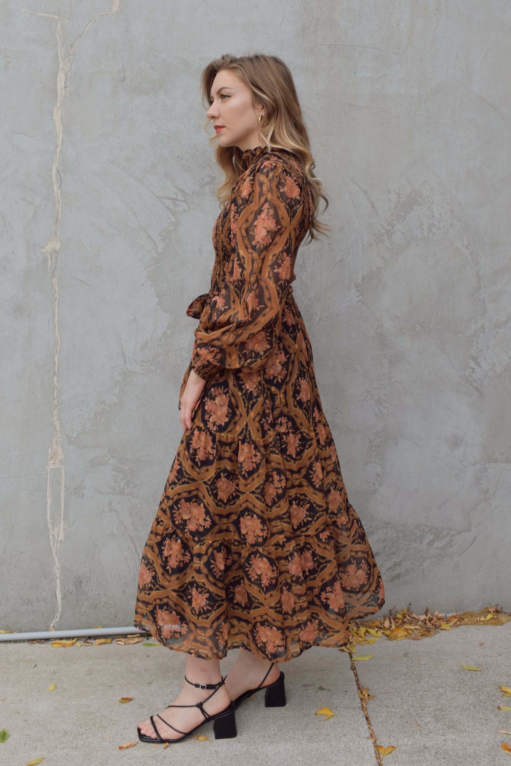 long sleeve high/mock neck midi dress with smocked bodice and cuffs, sheer sleeves, flowy skirt, fabric tie at waist, floral boho tapestry pattern. double button at back of neck