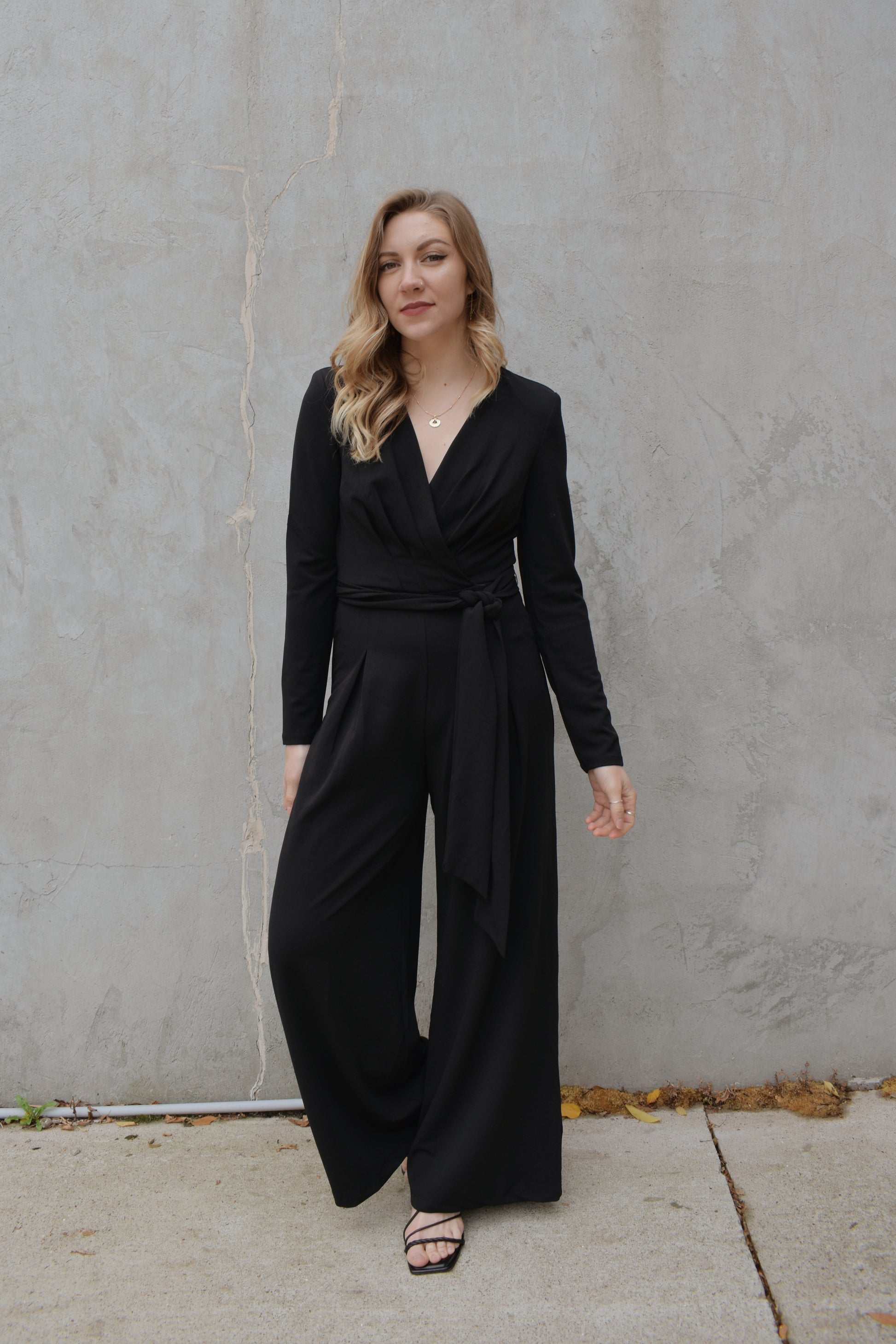 black wide leg long sleeve jumpsuit with wrap effect and fabric tie. pleated v neck with fitted arms and zip back enclosure