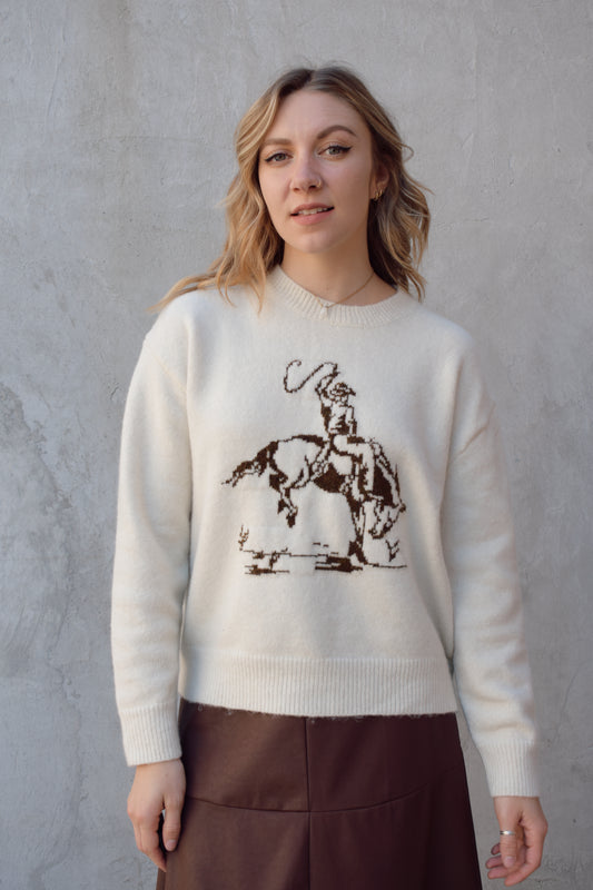 cream colored crew neck sweater relaxed fit full length with cowboy design in brown on front ribbed cuffs hem and neckline