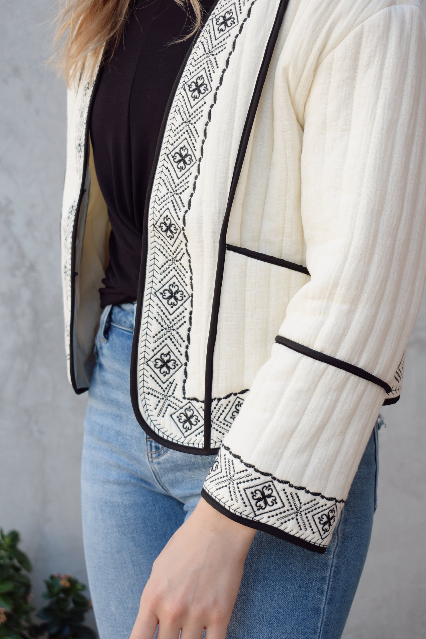 boho quilted ivory jacket with black exposed seam detailing and design along hem, has pockets, 2 clasp enclosure 